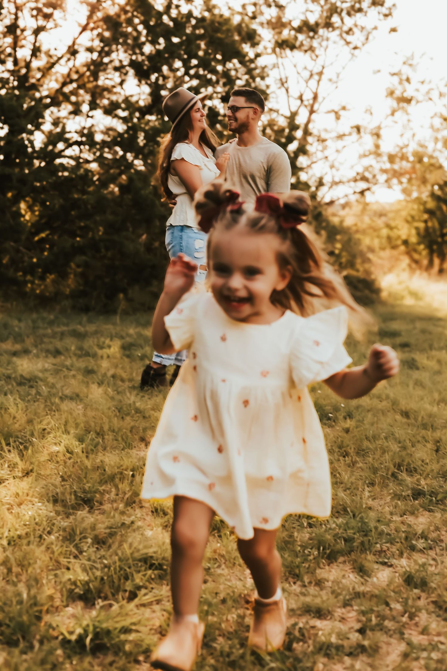 A young child dances joyfully in a white dress while a roller-skating couple shares a moment in the sunset-lit field.