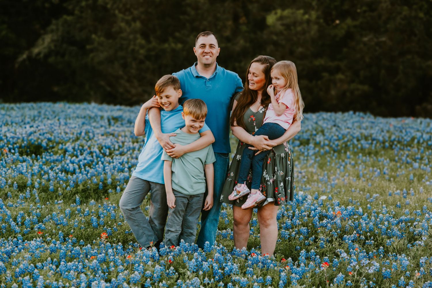Family smiling together in field of blooming blue wildflowers during spring photo session.