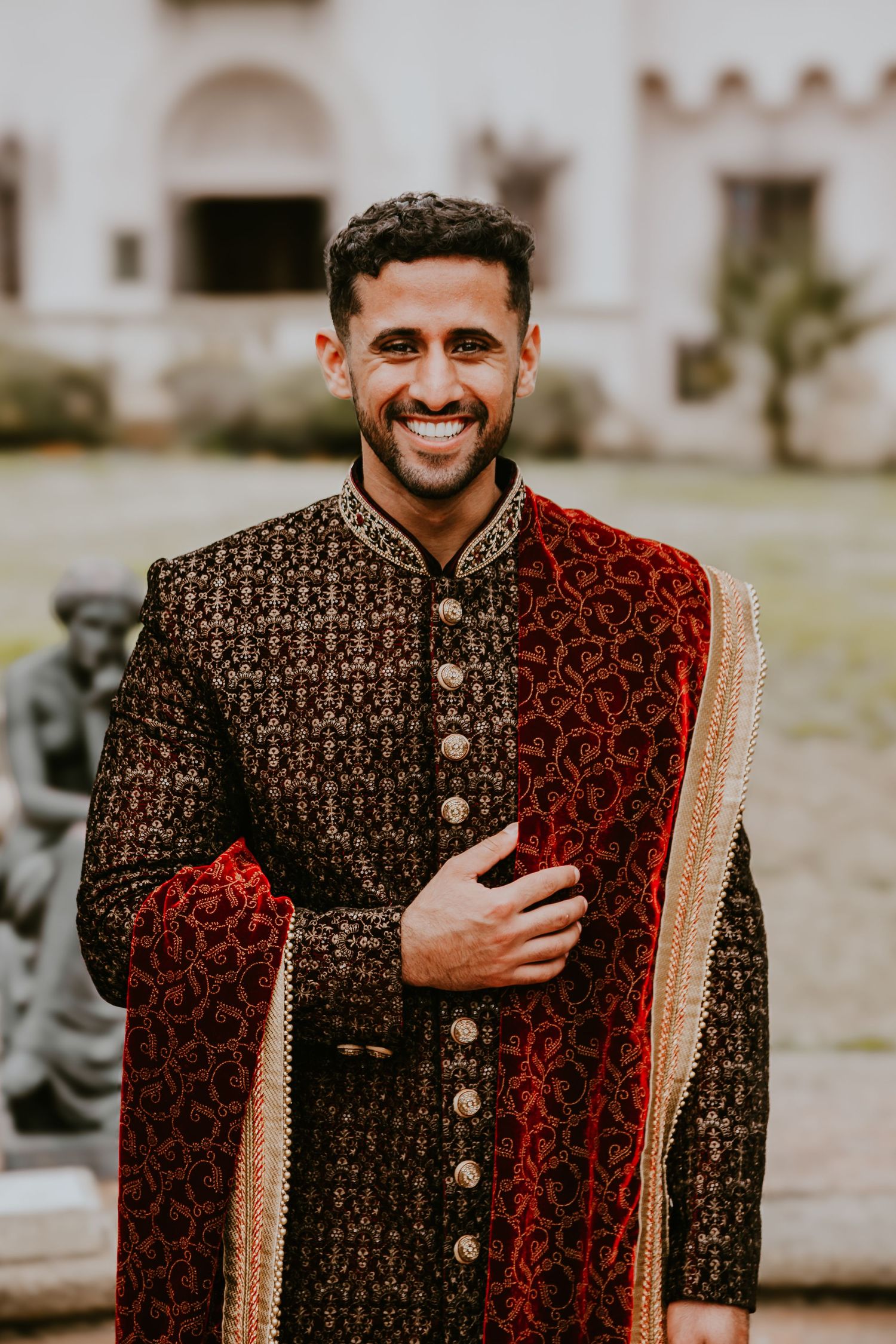 Elegant South Asian groom wearing a traditional two-toned black and red sherwani with golden embroidery and buttons.
