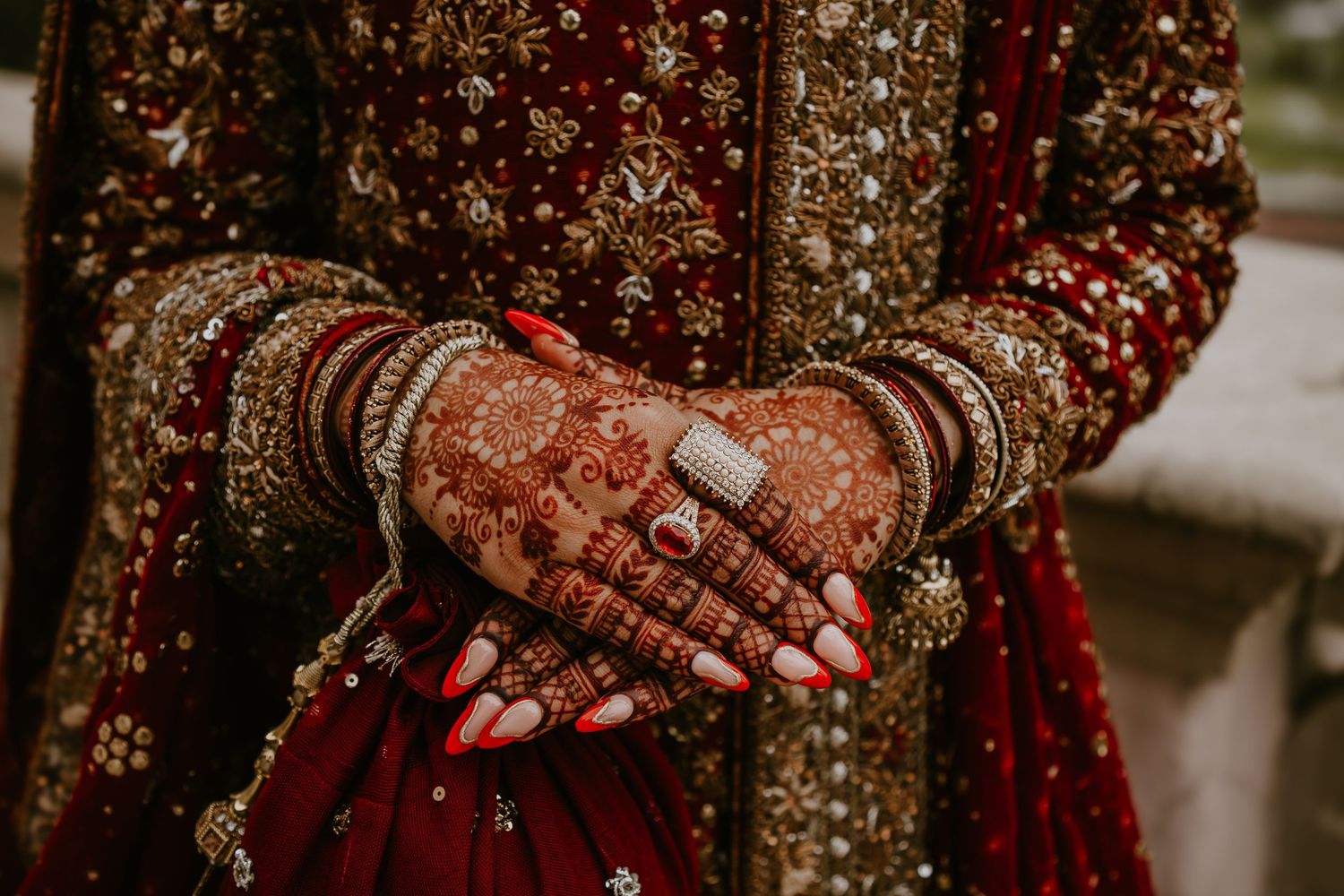 Close-up shot of traditional Indian bridal hands adorned with red mehndi and gold bangles against a red lehenga.