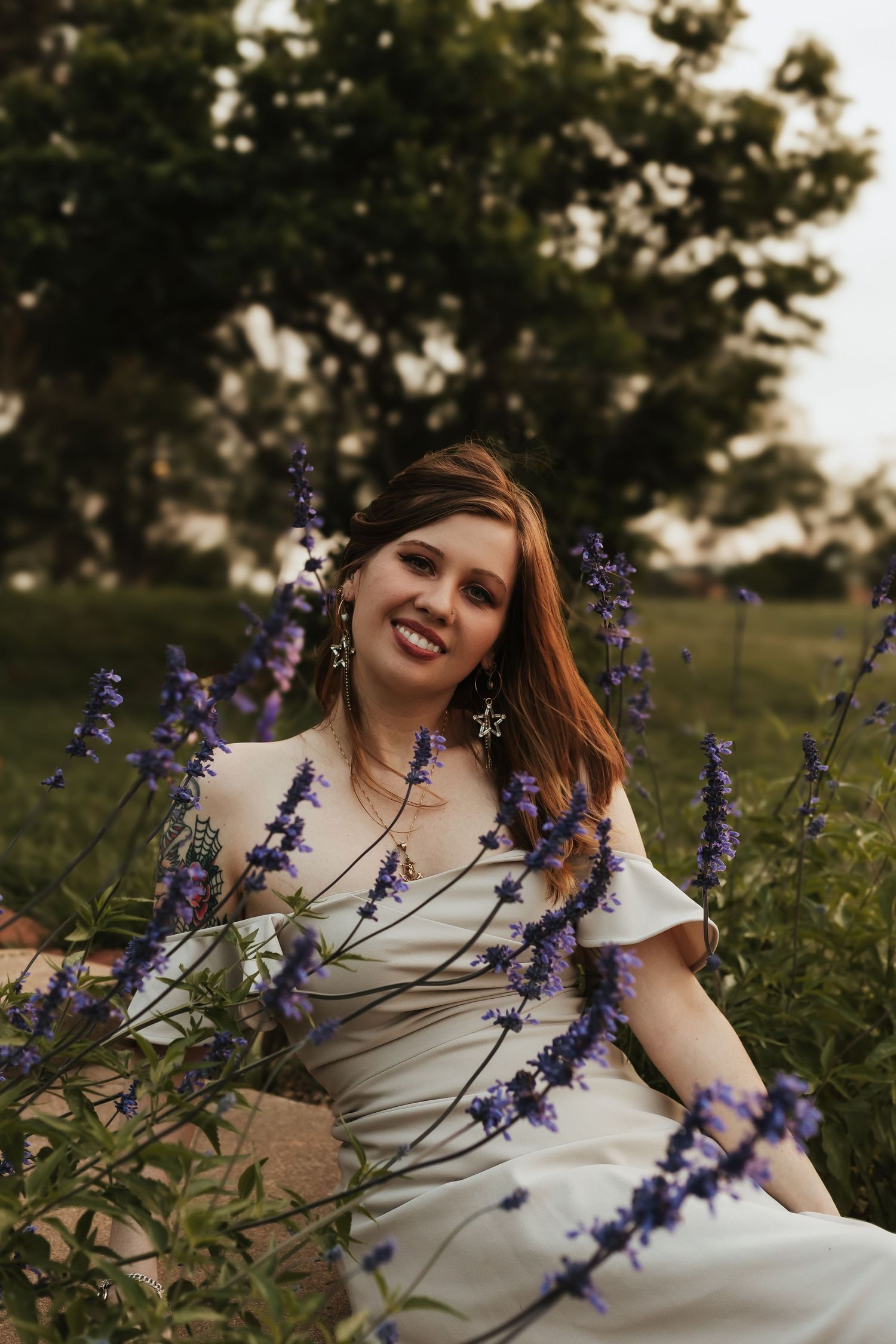 A person in a white dress sits among blooming purple wildflowers in a golden hour nature setting.
