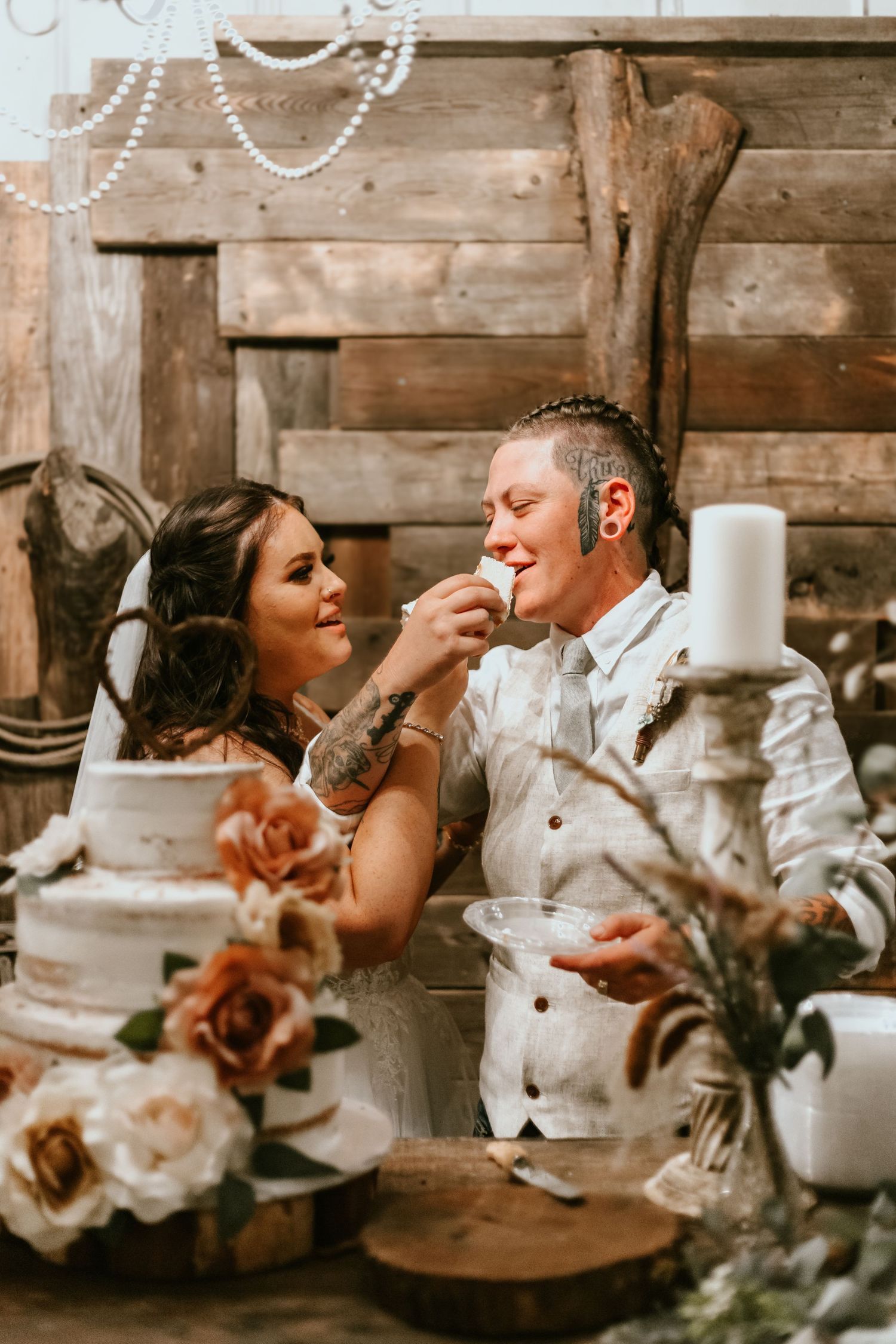 A rustic wedding celebration features a couple sharing cake at their reception with wooden decor and floral arrangements.