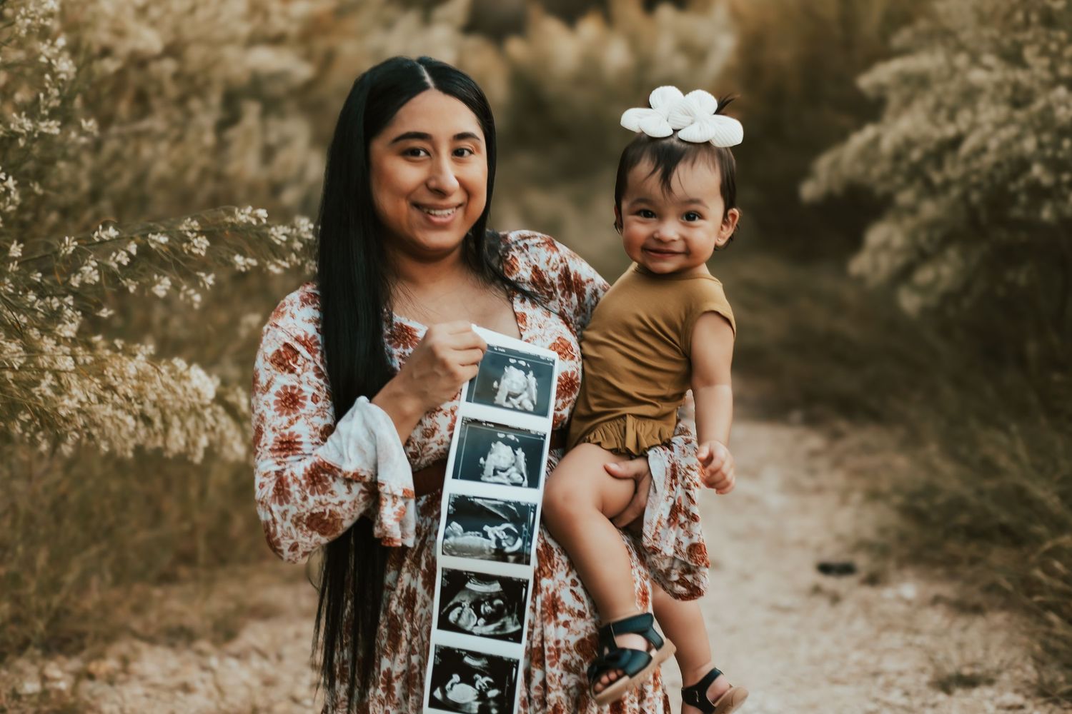 A pregnancy announcement photo series showing ultrasound pictures in a warm outdoor setting with fall foliage.