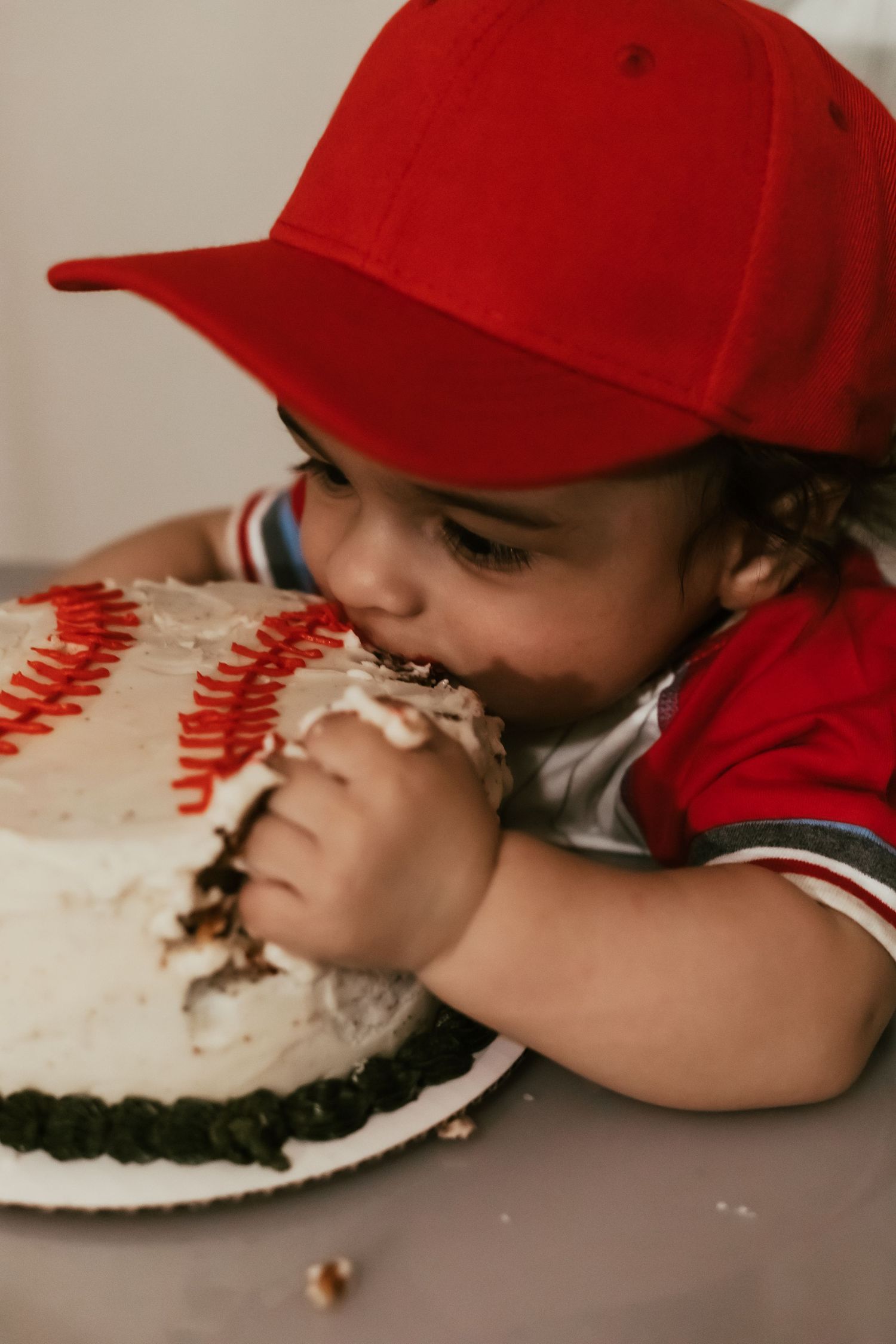A young figure in a red baseball cap lays on their stomach while eating from a white plate on the floor.