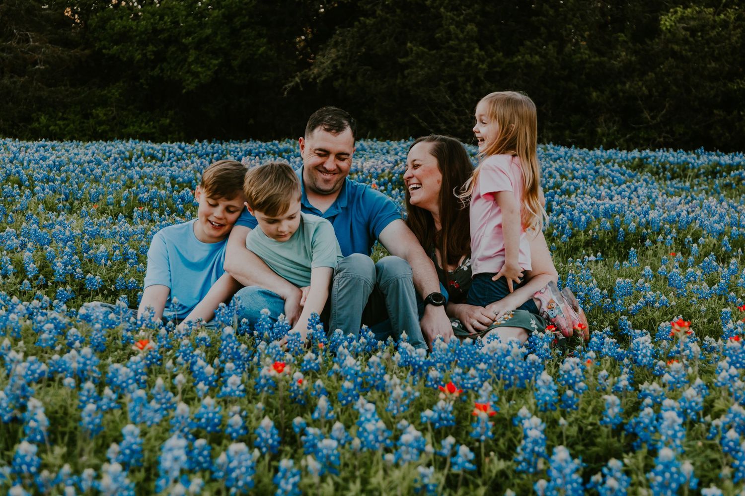 A family relaxes together in a beautiful field of vibrant blue wildflowers during springtime.