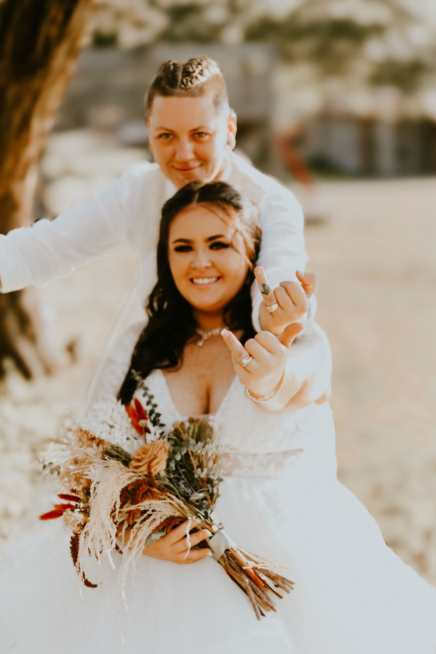 A joyful wedding couple embraces outdoors in warm sunlight with a rustic bouquet.
