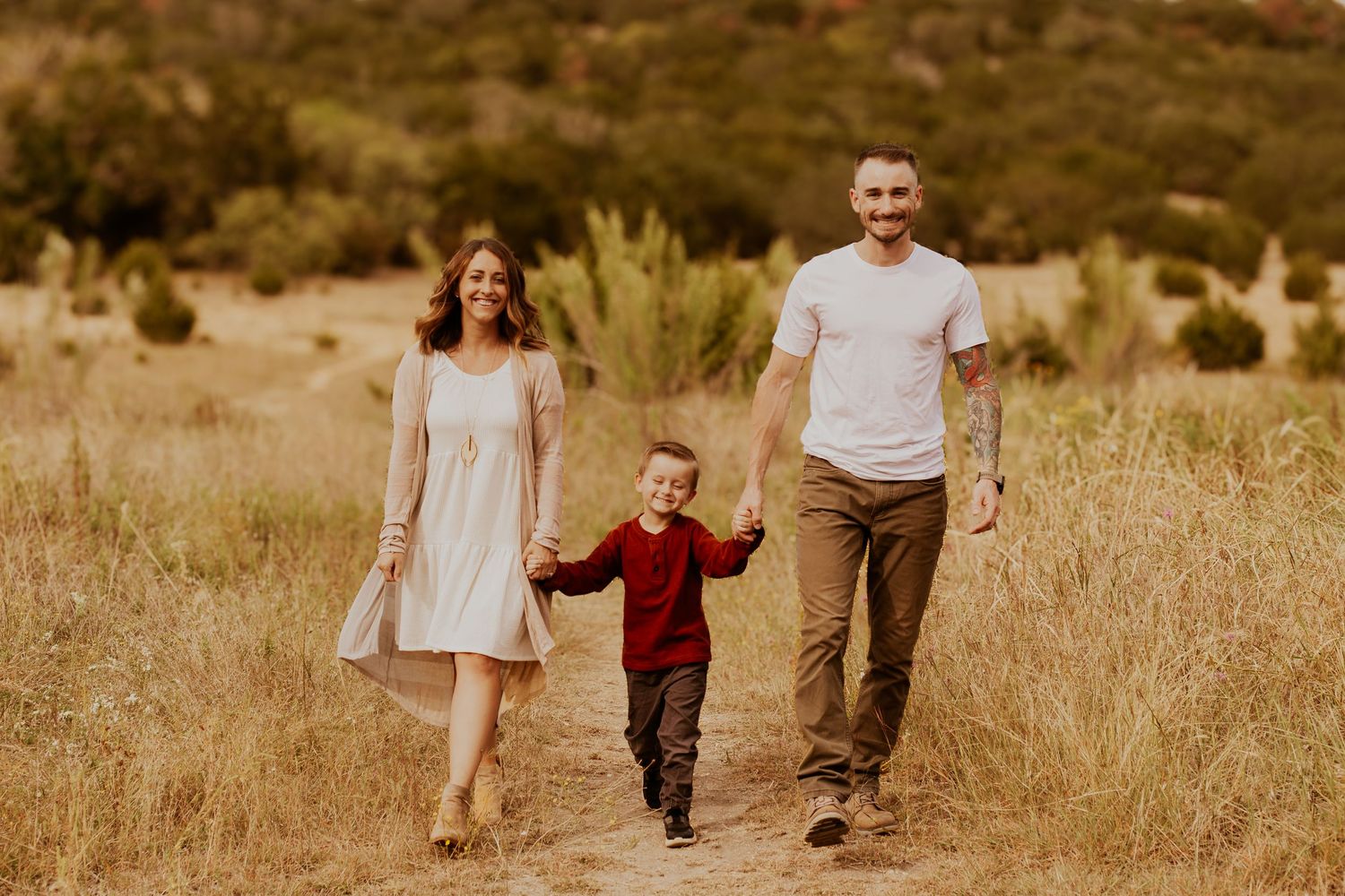 Family walks together holding hands through a golden field at sunset in warm autumn lighting.