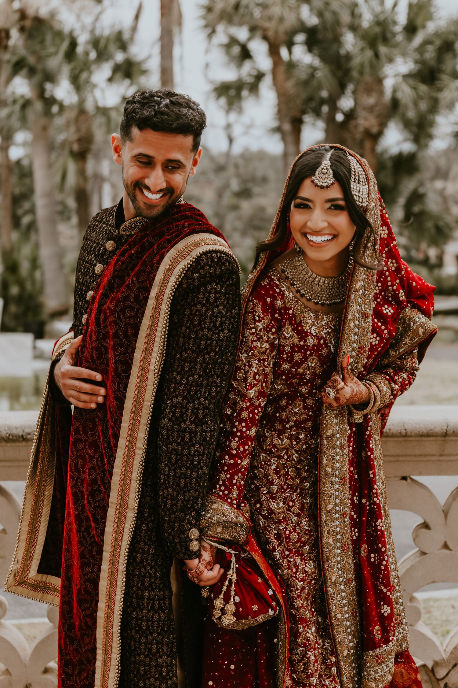 A couple in traditional Indian wedding attire share joyful moments during their outdoor photo session.
