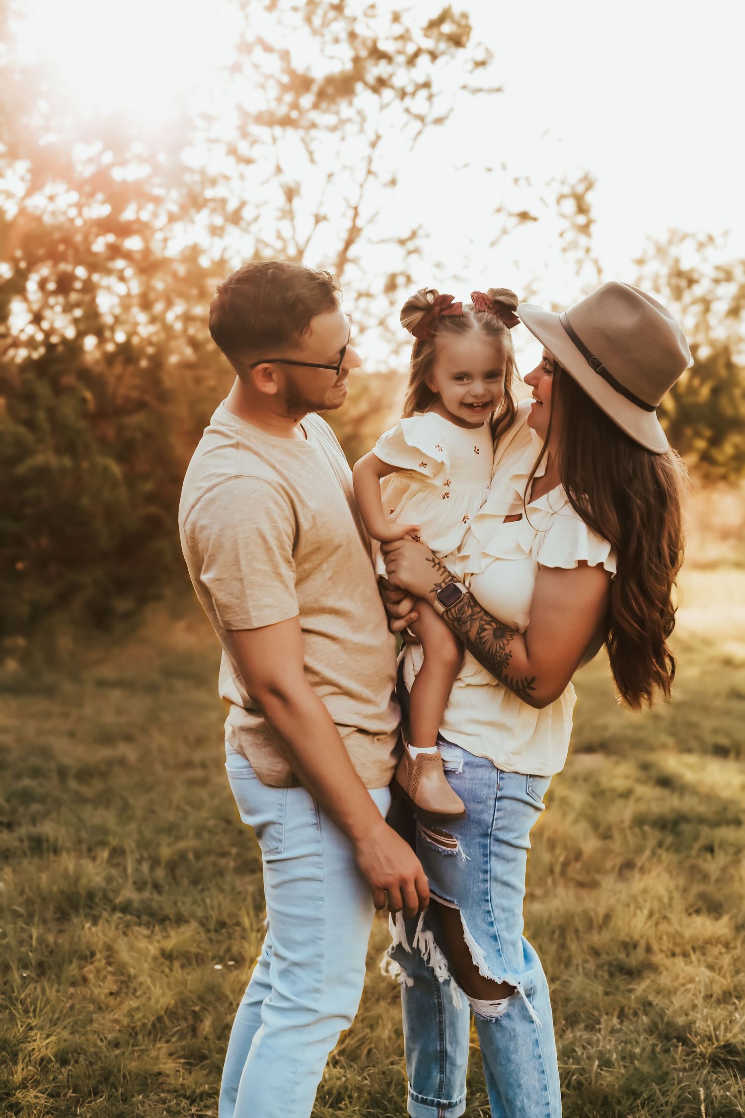 A family of three shares a sweet moment together outdoors during golden hour sunset in a field.