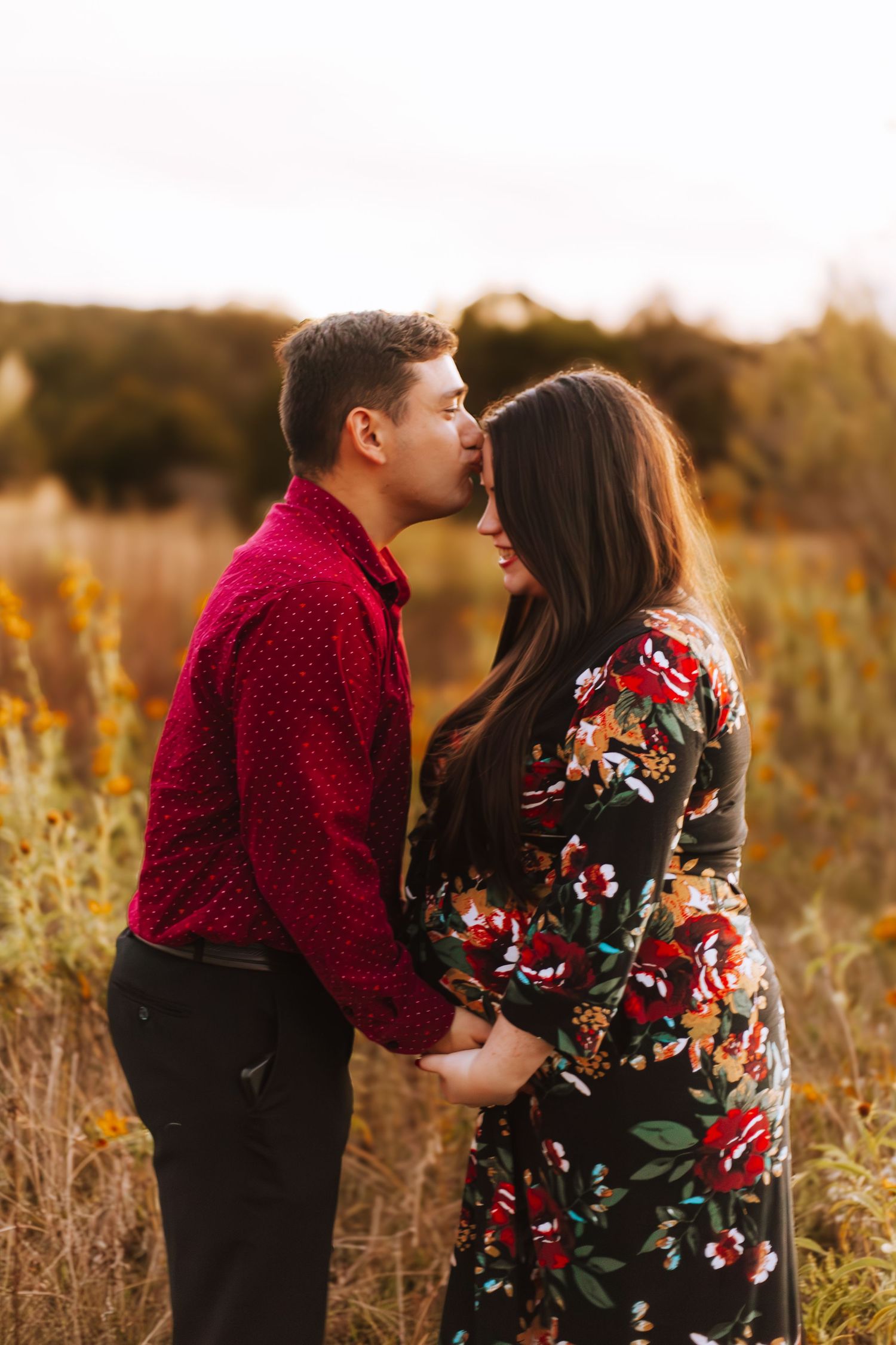 A romantic couple embraces in a golden field at sunset, with the person in red kissing their partner in a floral dress.