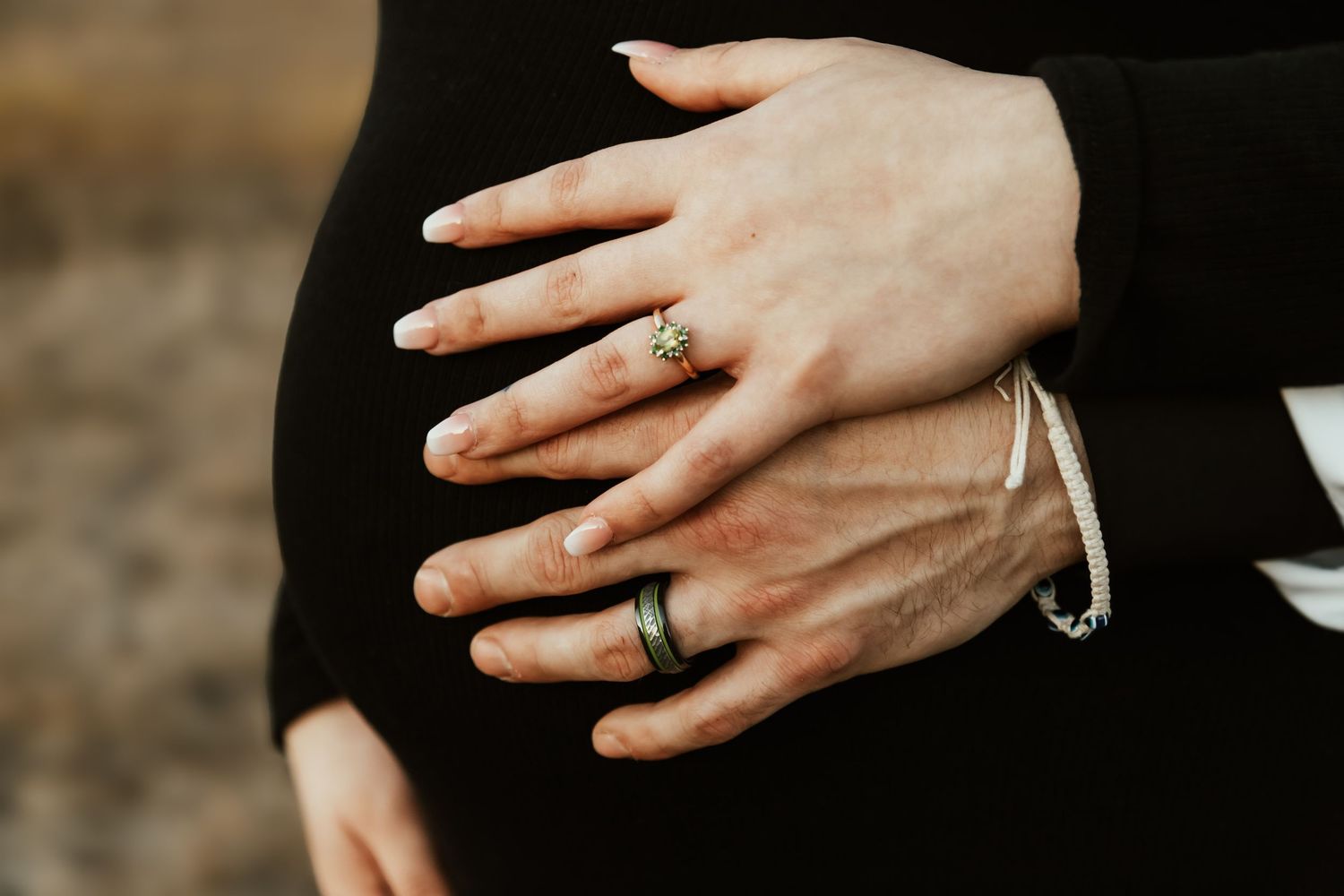 Close-up of hands wearing wedding rings against a black dress background.