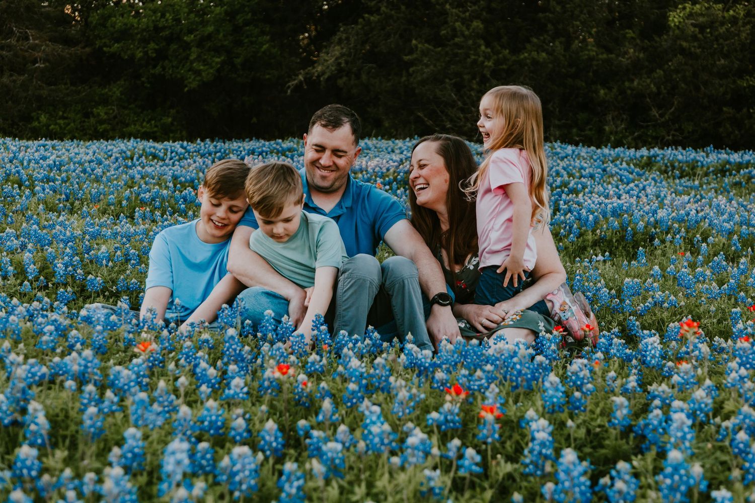 Family sitting together in field of vibrant blue wildflowers during springtime photo session.
