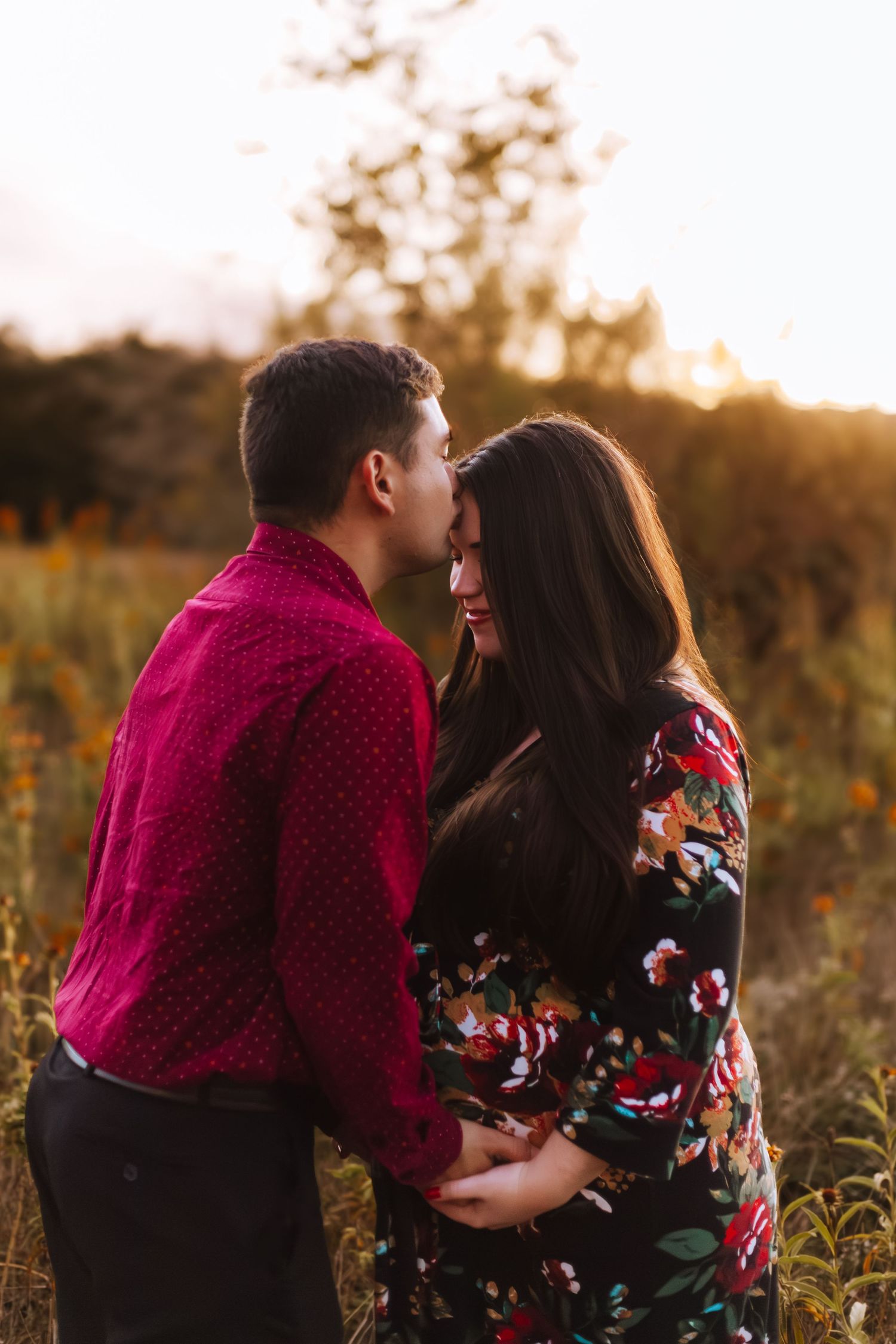 Intimate maternity portrait of couple in floral dress and red shirt during golden hour.
