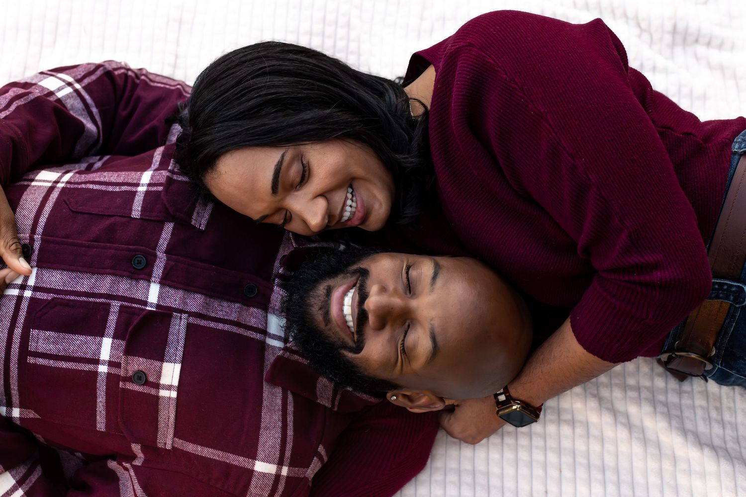 Couple laying down and laughing together on plaid blanket.