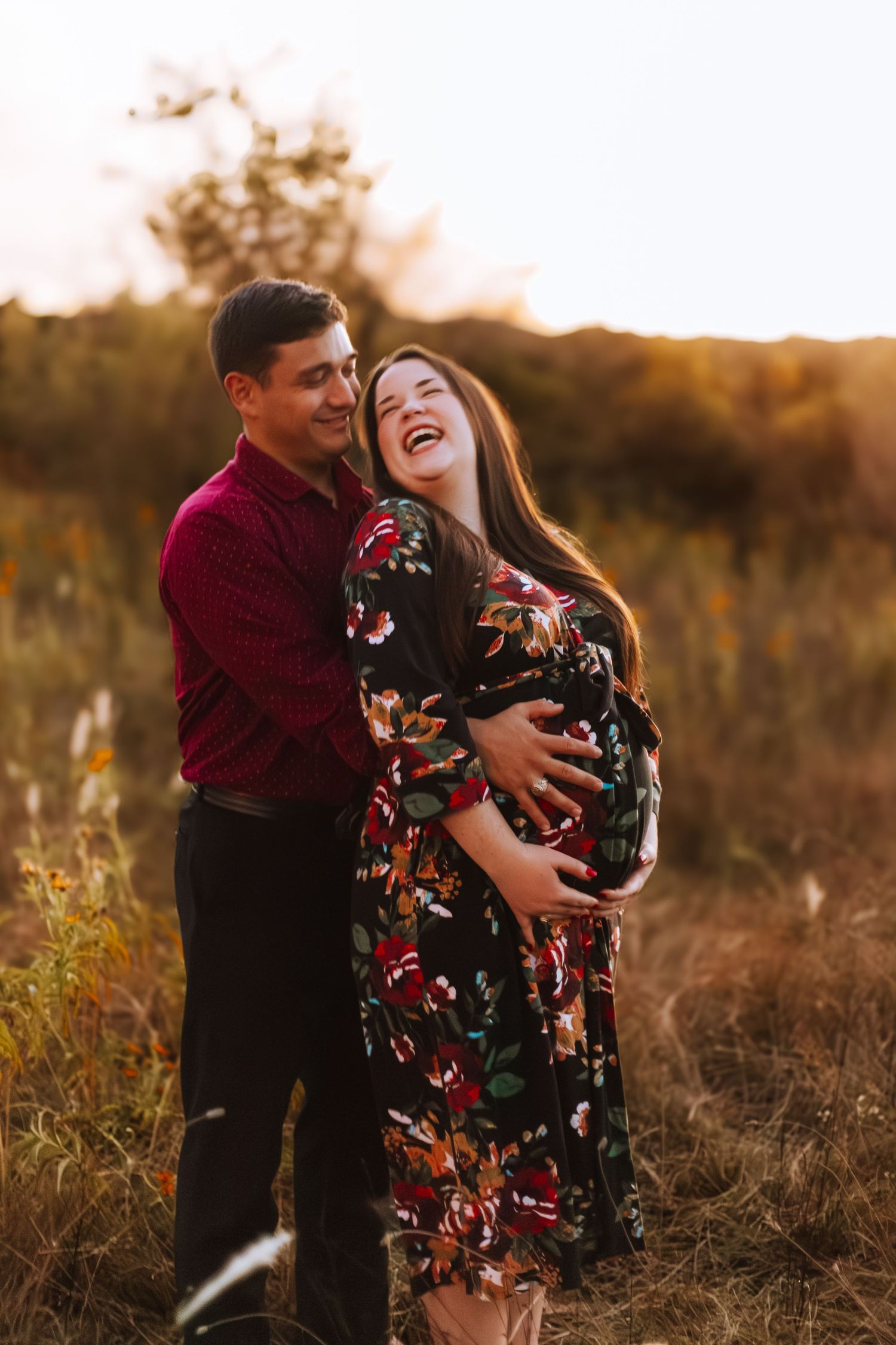 A couple embraces in a golden sunset field, sharing a joyful moment in autumn light.
