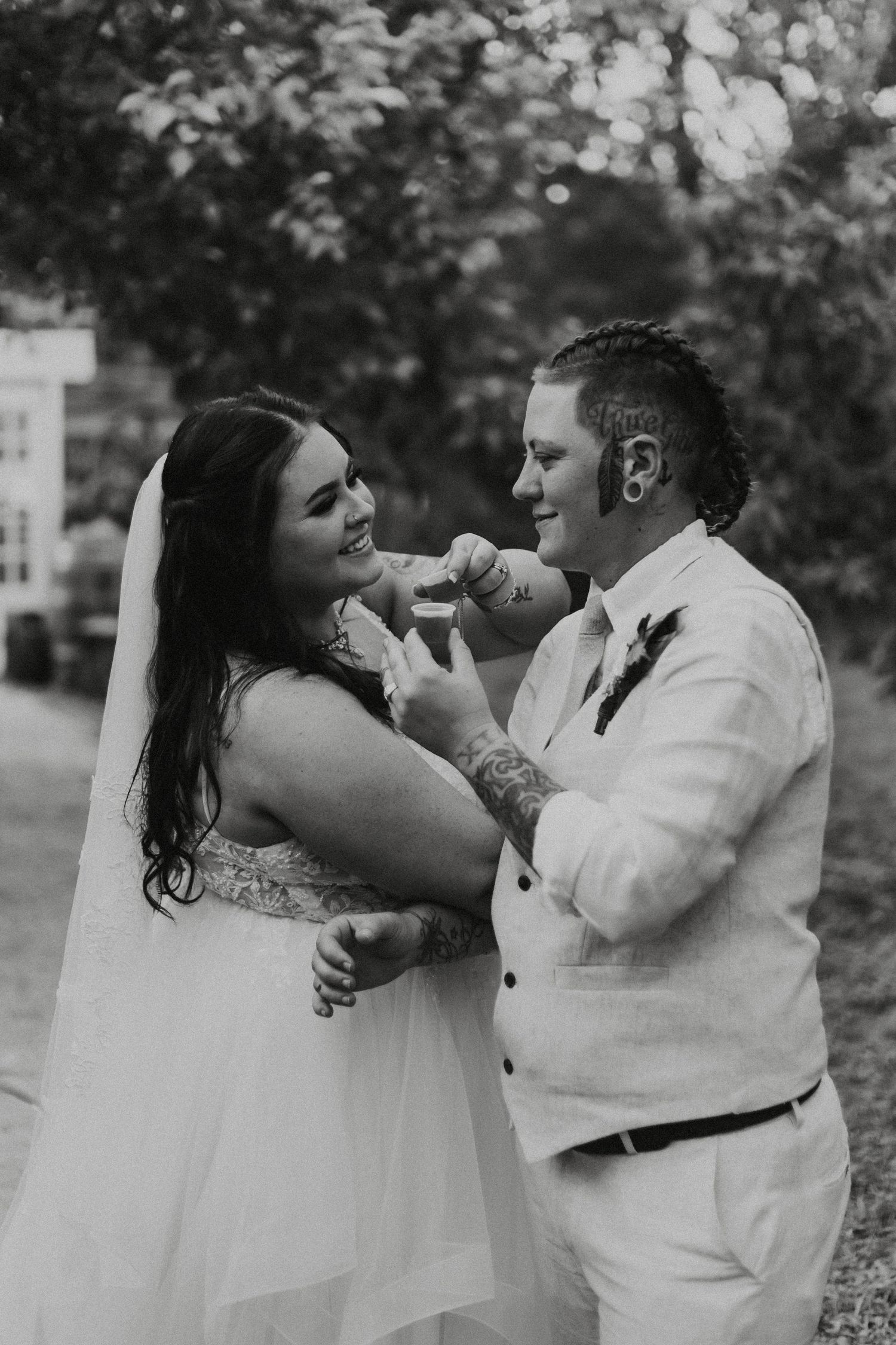 Fun black and white wedding photo of a couple playfully feeding each other during their outdoor celebration.
