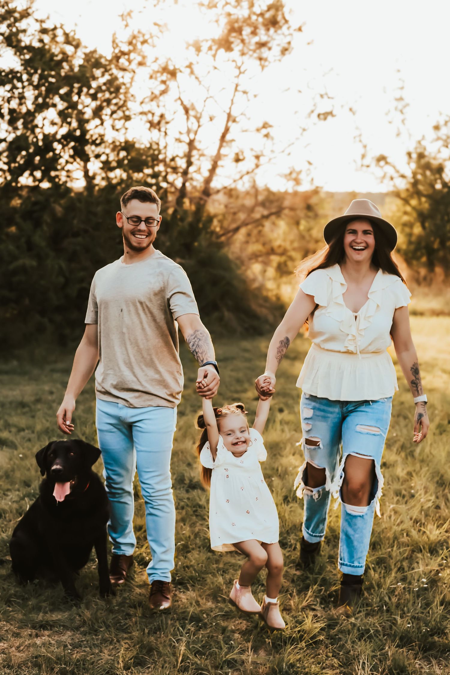 Family walks together with their black dog in a golden sunset meadow while holding hands and smiling.