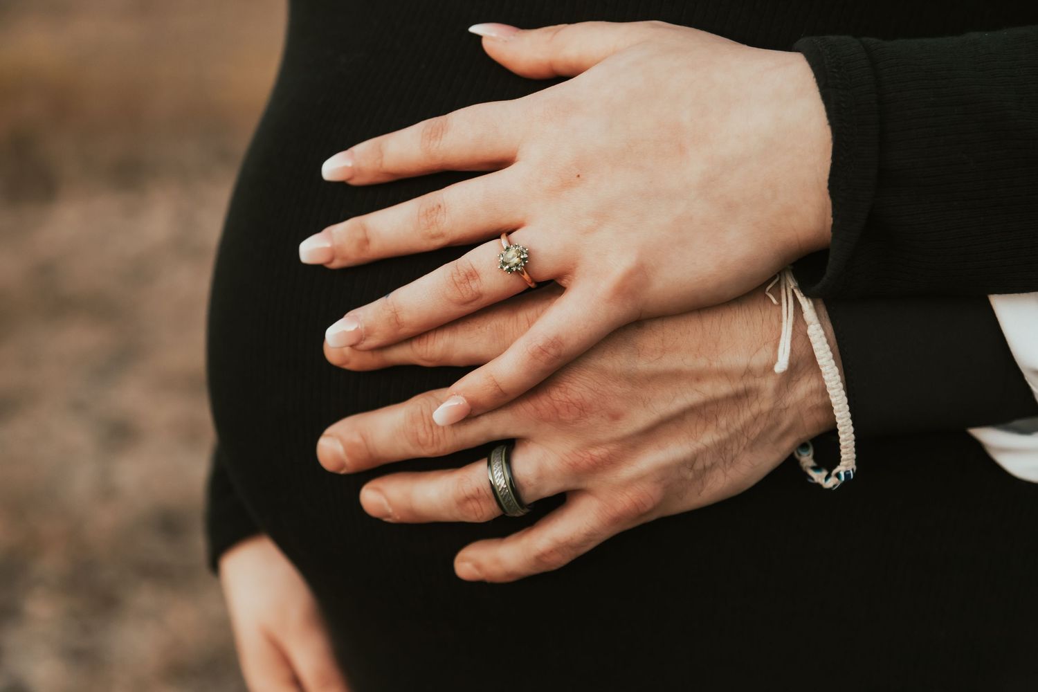 Close up of hands with wedding rings resting on a pregnant belly in black clothing.