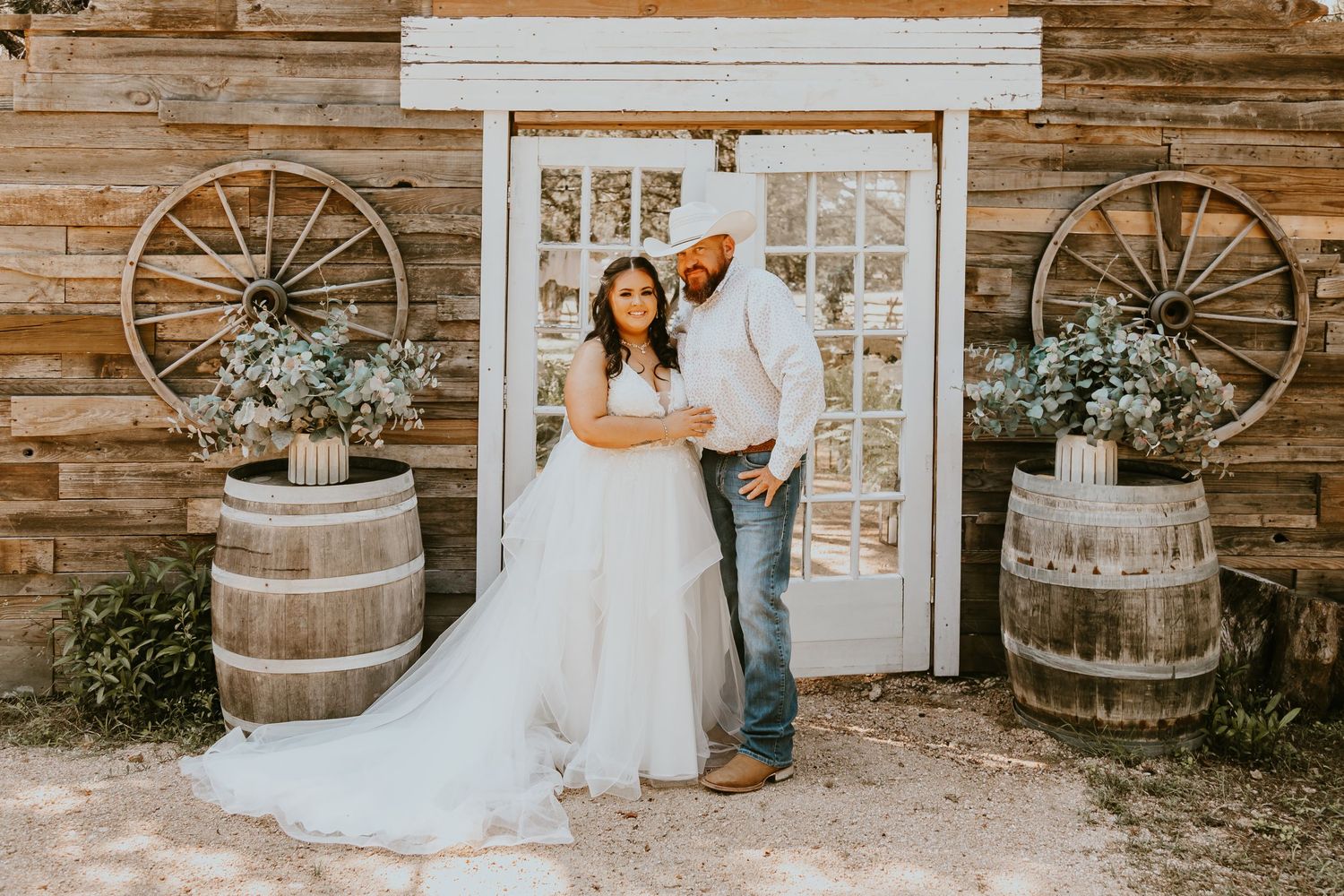 A rustic barn wedding scene with wagon wheel decor, wooden barrels, and delicate floral arrangements.
