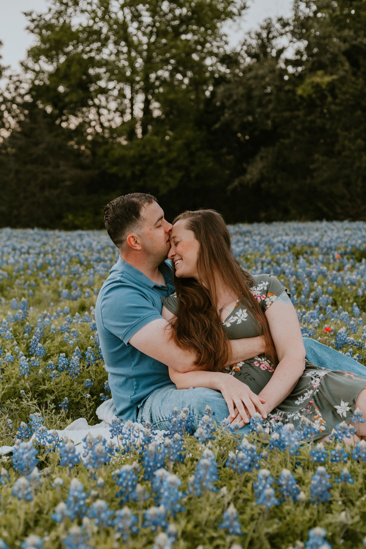 A couple shares a romantic moment while sitting in a field of blooming blue wildflowers at sunset.