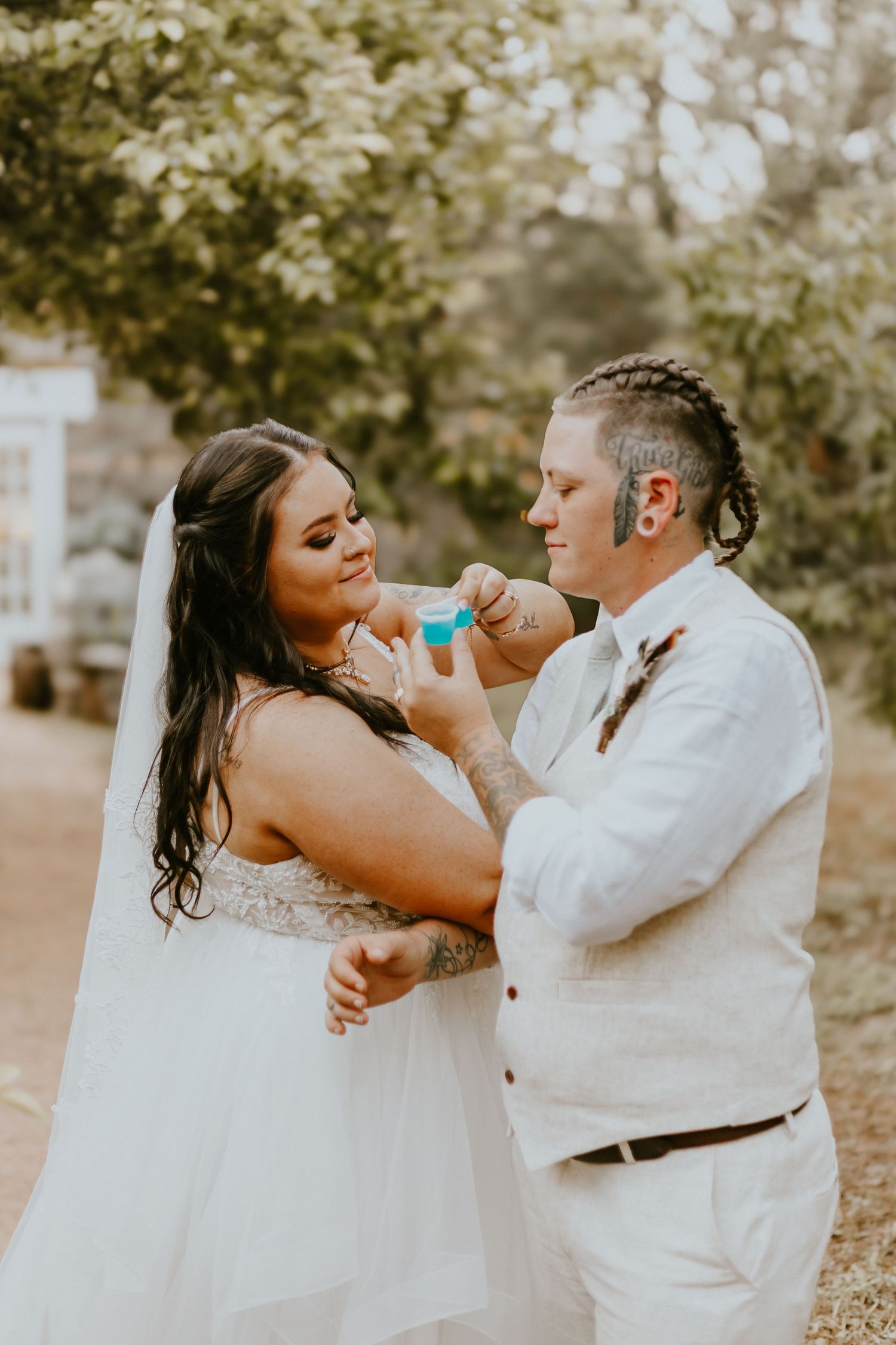 A couple shares a playful moment during their wedding photoshoot in an outdoor setting with natural bokeh in the background.