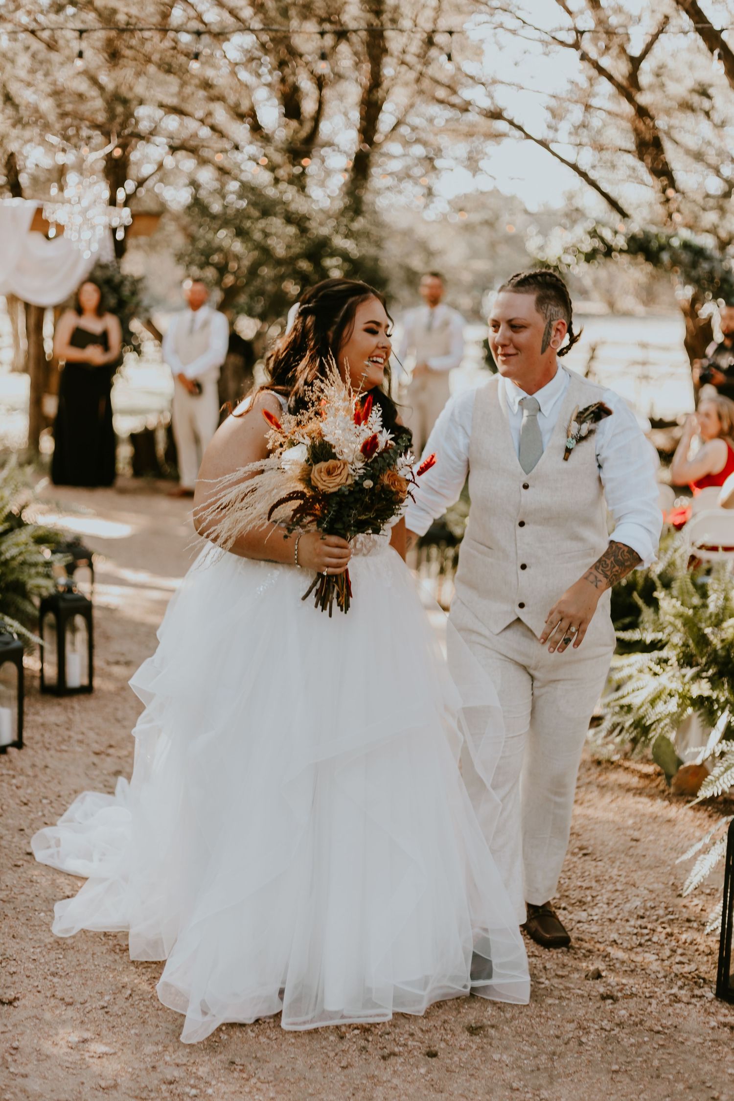 A joyful couple dances in flowing white attire beneath sunlit autumn trees during a romantic outdoor celebration.
