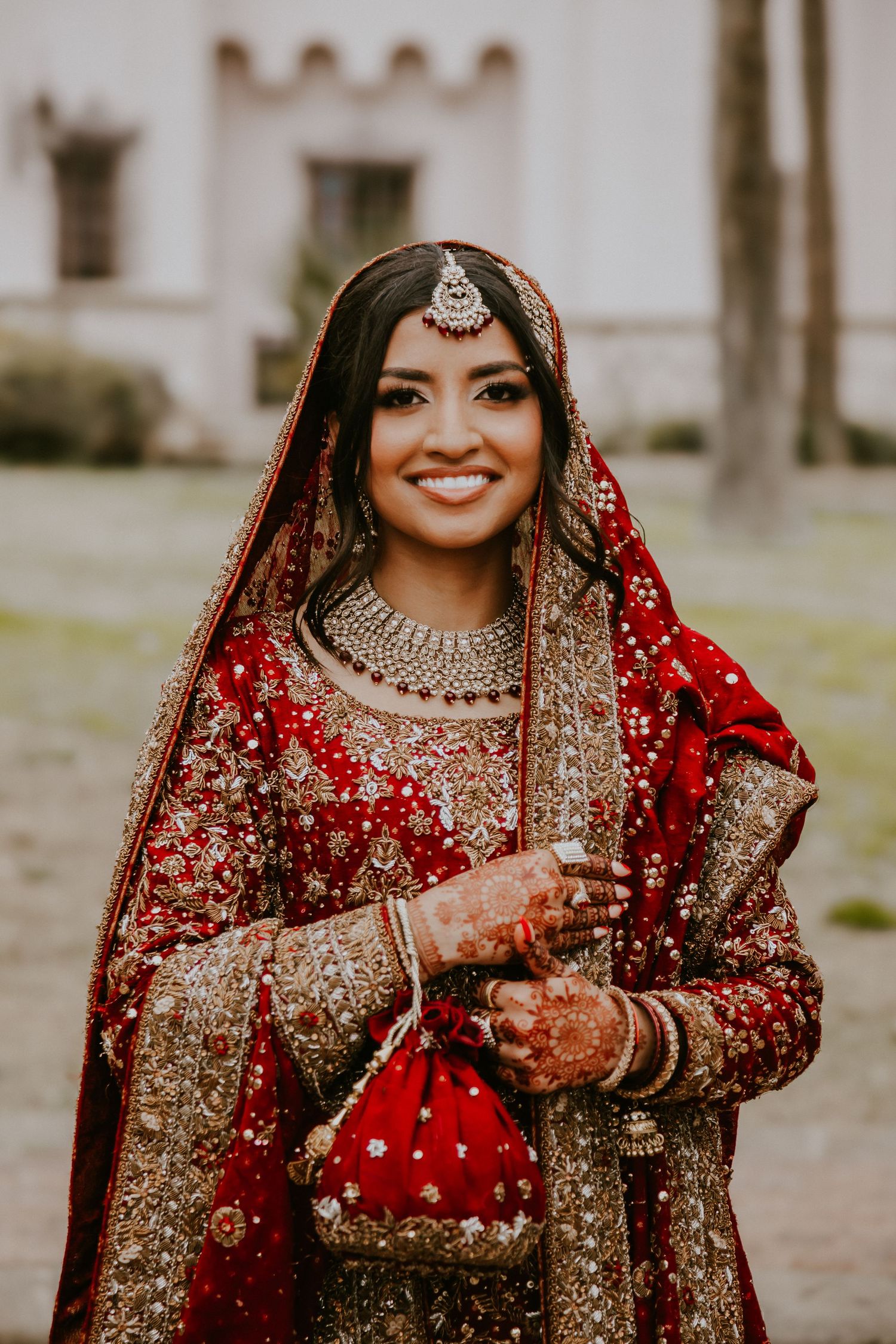 Beautiful traditional South Asian bride in ornate red and gold lehenga with jewelry and henna adorned hands.