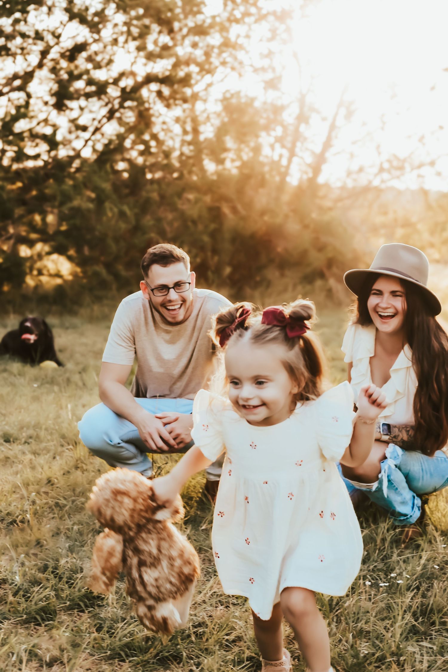 Young family playing outdoors at sunset in a grassy field with their small dog during a warm golden hour.