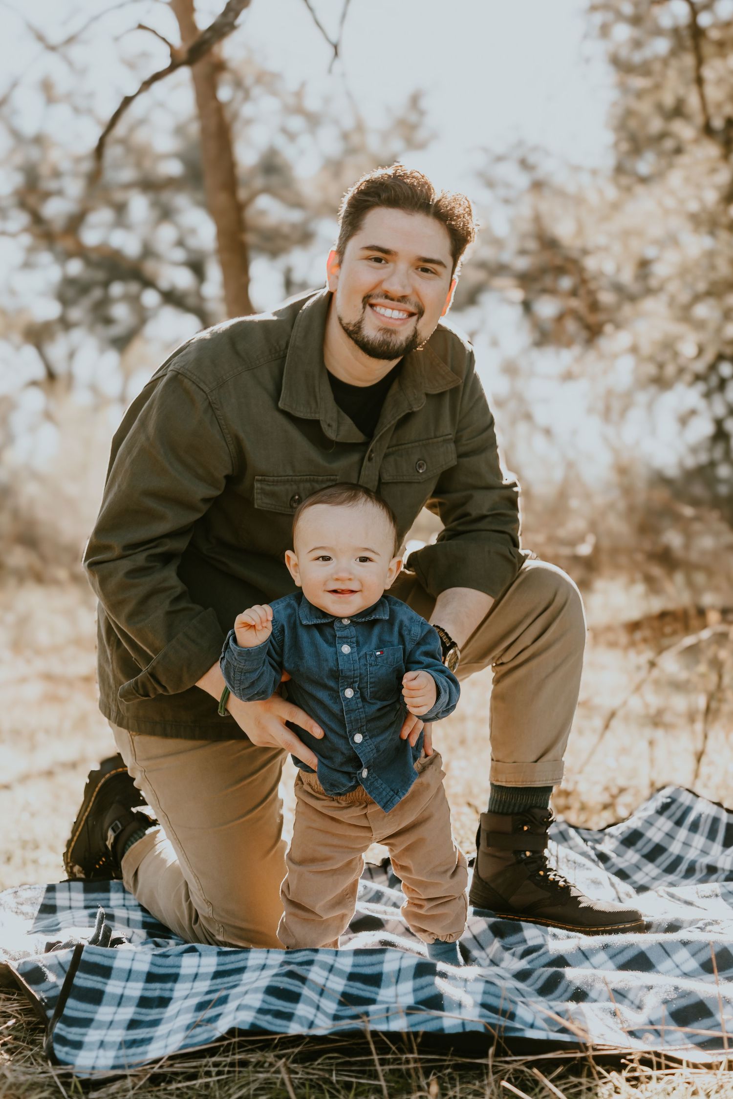 A candid outdoor family portrait on a plaid blanket during autumn with warm lighting and natural woodland backdrop.