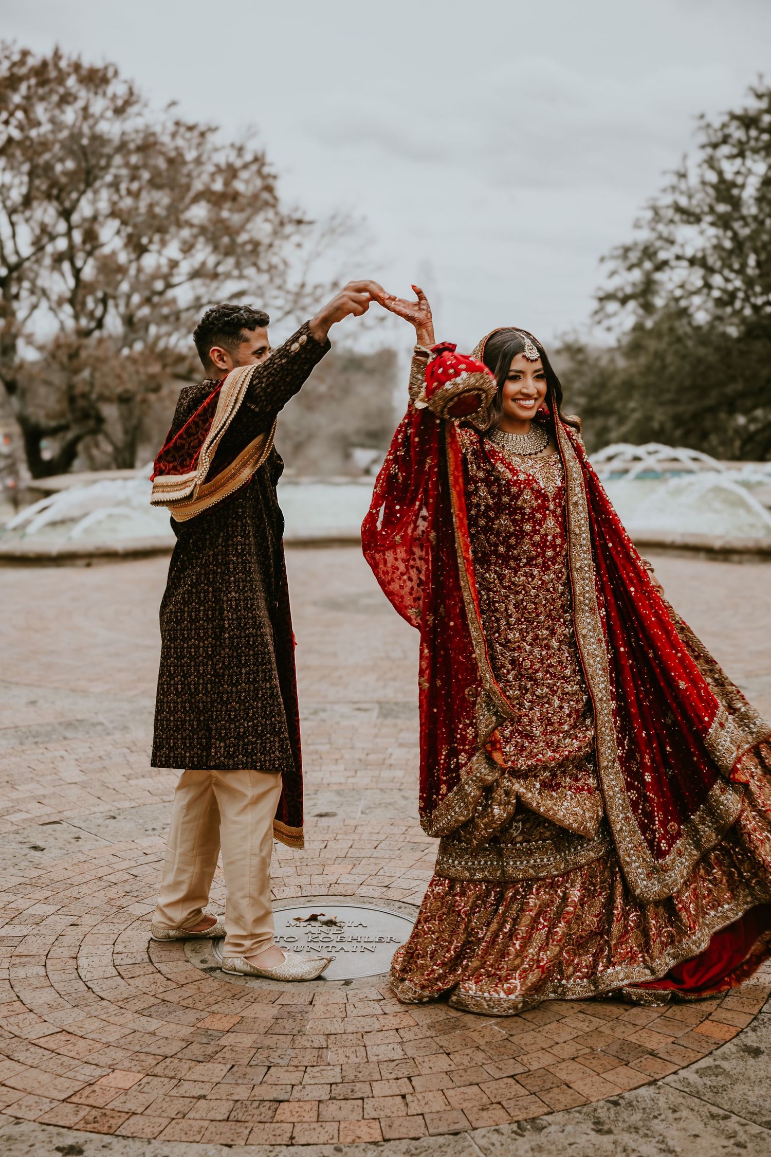 A couple in traditional South Asian wedding attire dance together on a brick patio during their celebration.