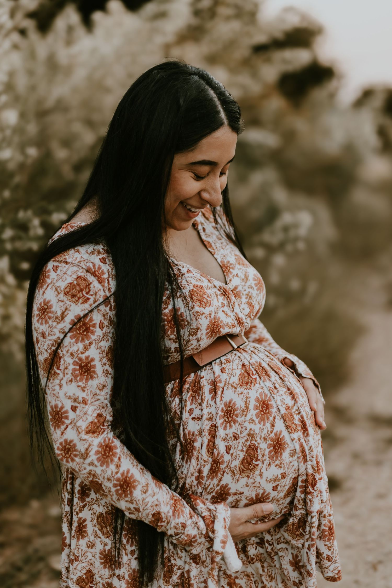 Maternity photoshoot series of an expectant mother in a floral dress showing her growing baby bump in natural lighting.