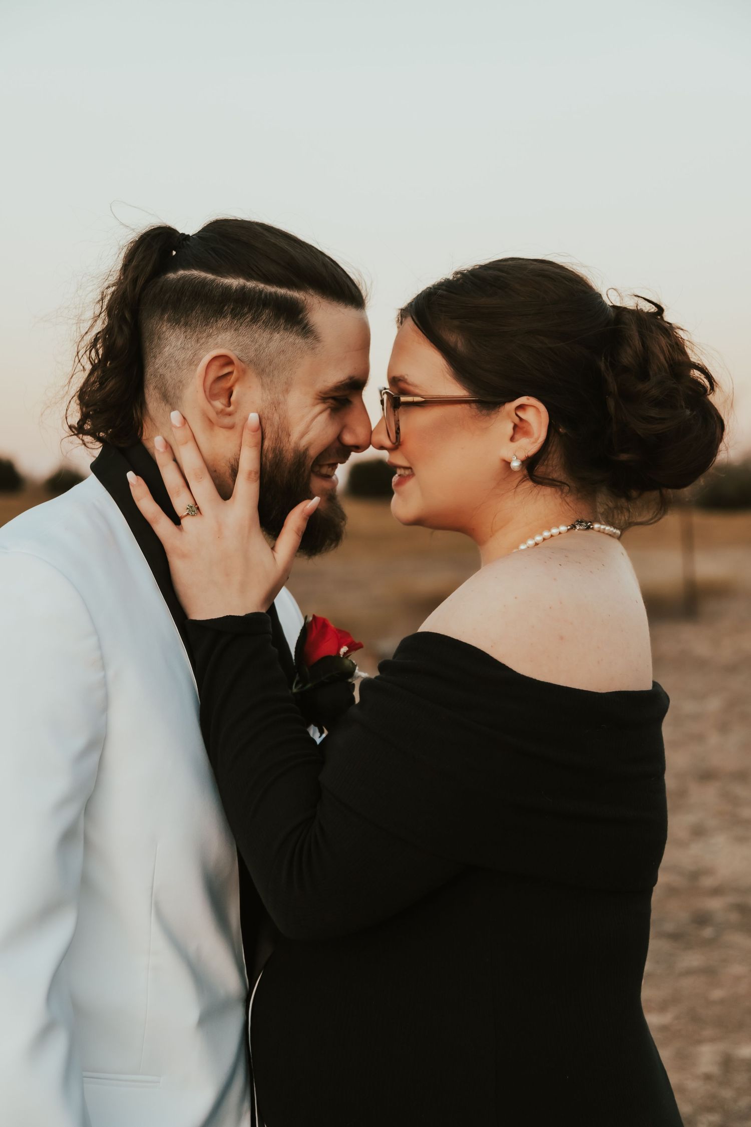 Romantic couple sharing an intimate moment at sunset, with her in black and him in white formal wear.