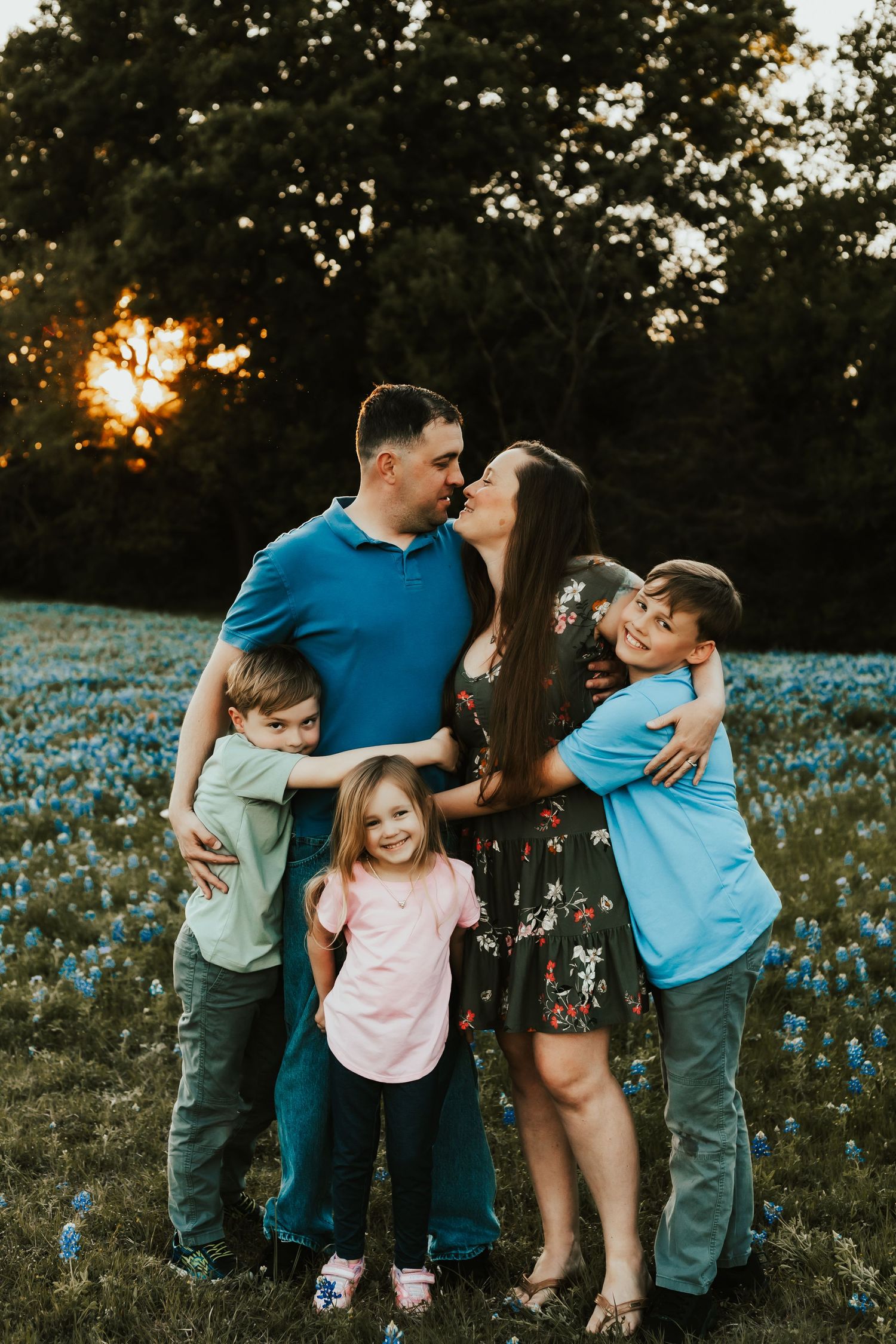 Family poses together in bluebonnet field during golden sunset in Texas.