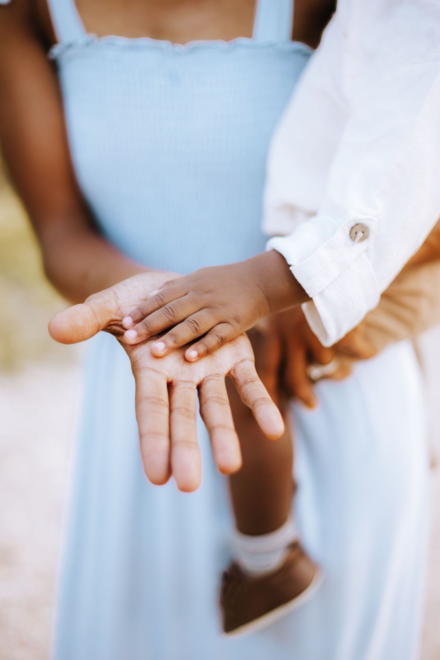 Close-up of hands tenderly touching, with person wearing light blue dress and white sleeve visible.