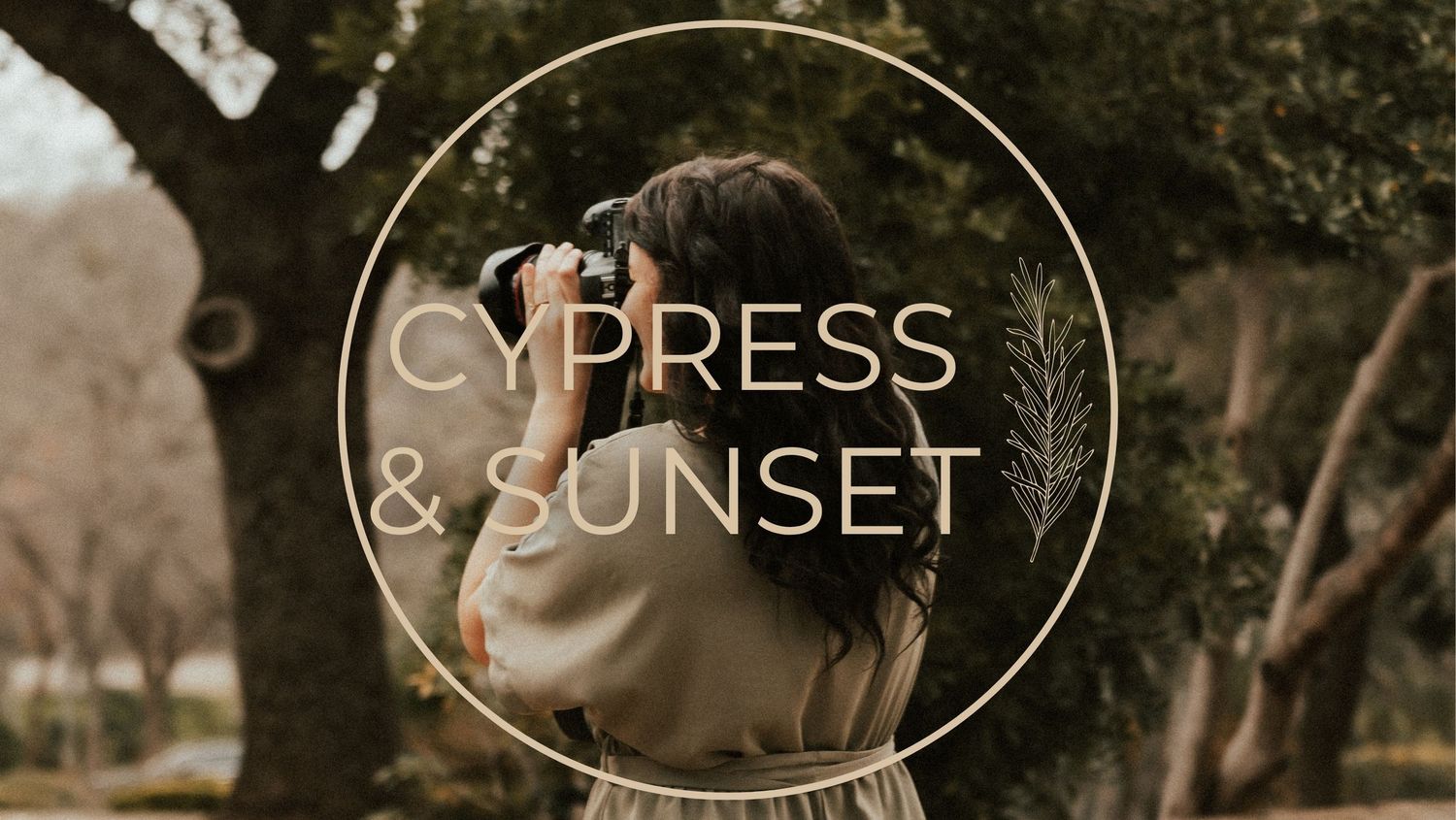 The photographer wearing sage green clothing takes a photograph outdoors with a circular Cypress & Sunset logo overlay design.