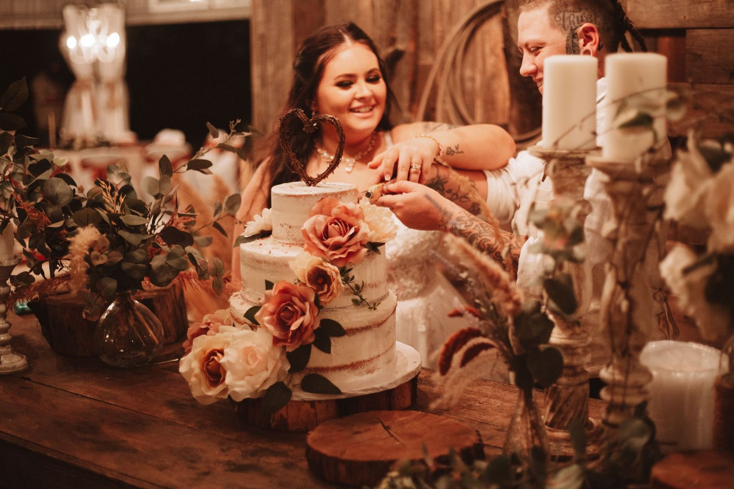 A person arranges peach and coral colored flowers on a rustic wooden table with candlelight in warm evening ambiance.