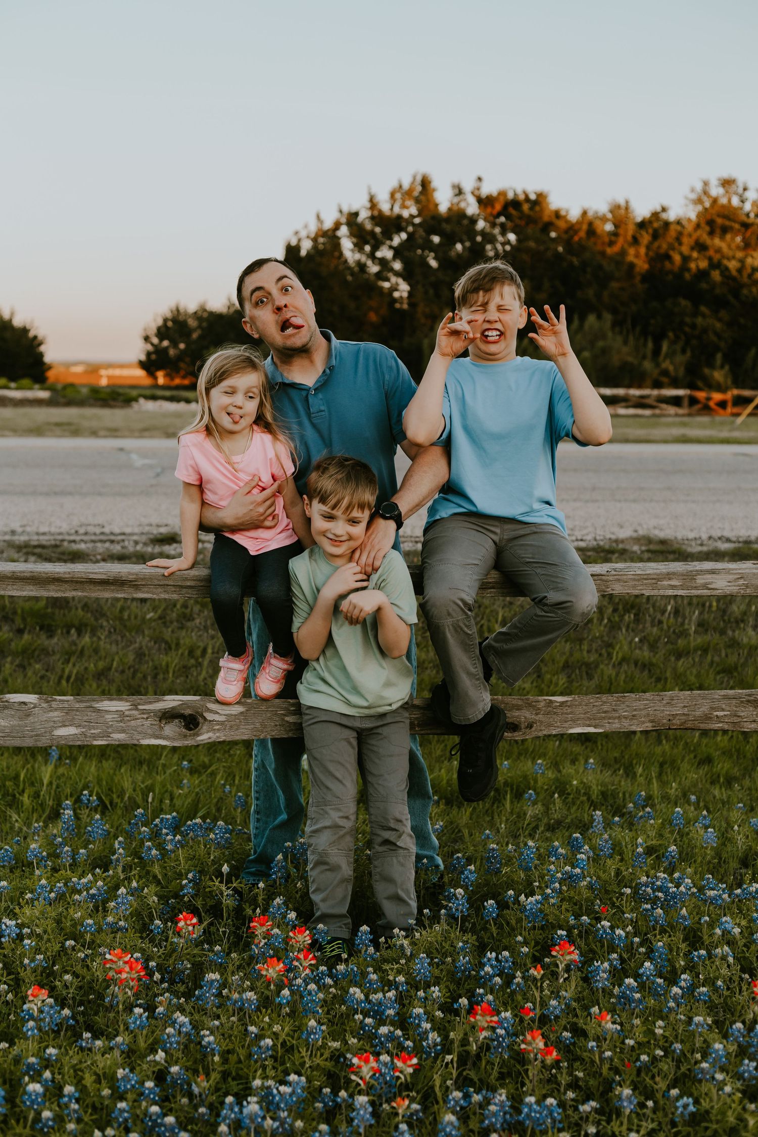People sitting on wooden fence surrounded by vibrant Texas wildflowers during golden sunset light.