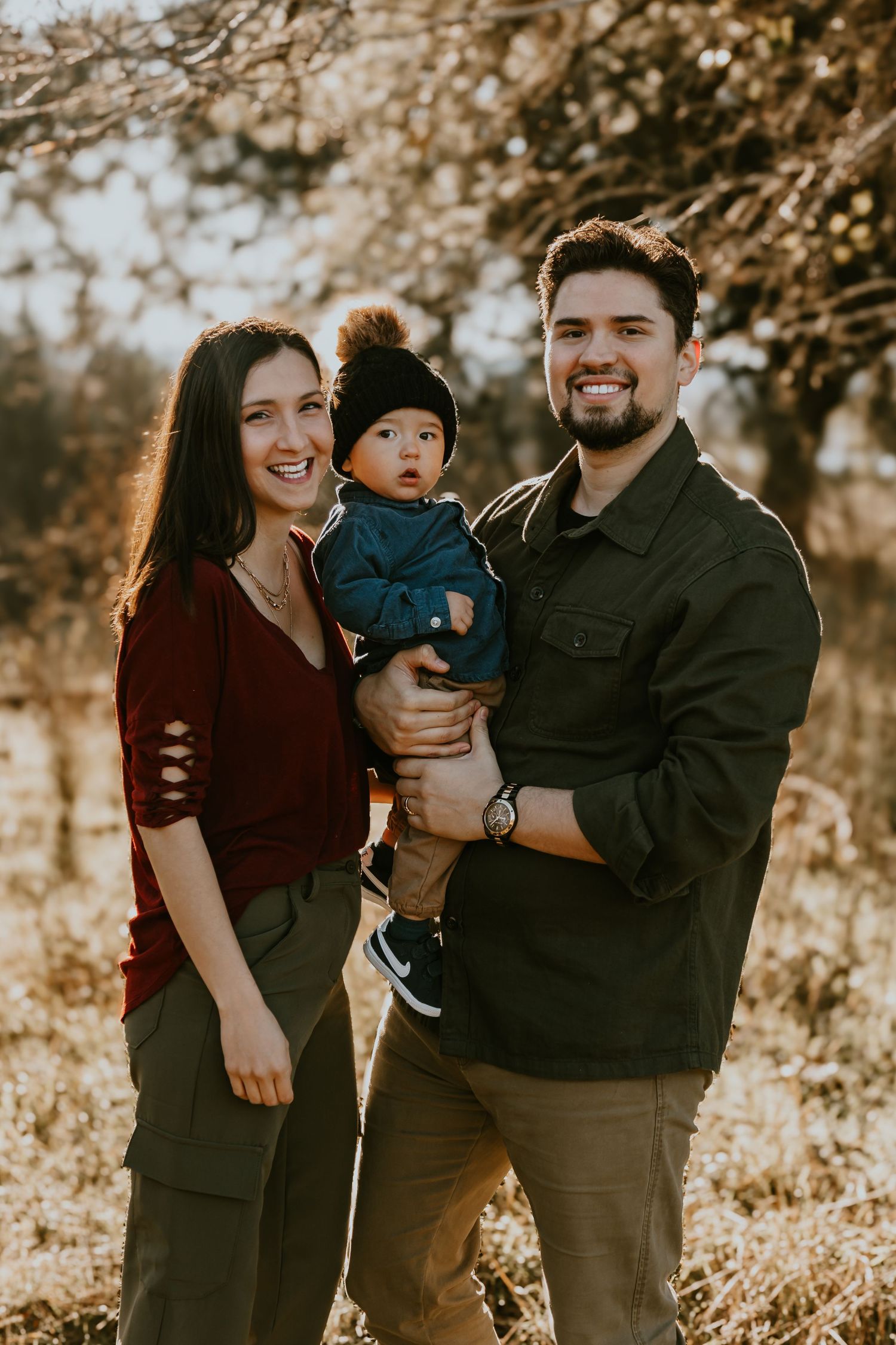 A young family poses together outdoors during golden hour in autumn amongst fallen leaves.