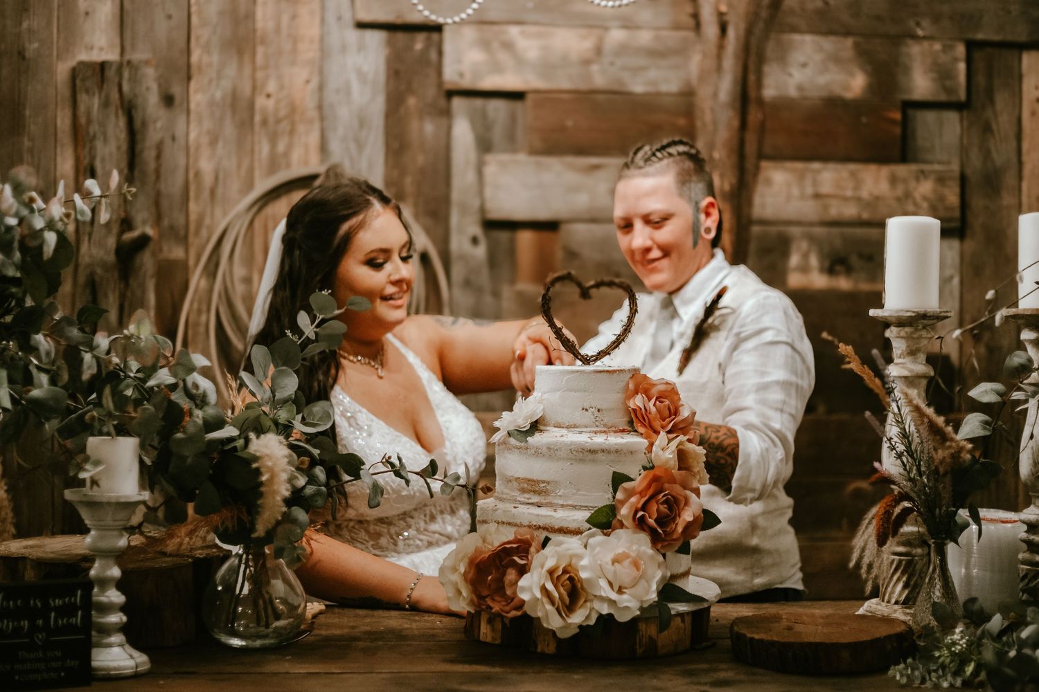 Two newlyweds share a joyful moment while cutting their wedding cake at their rustic barn reception.