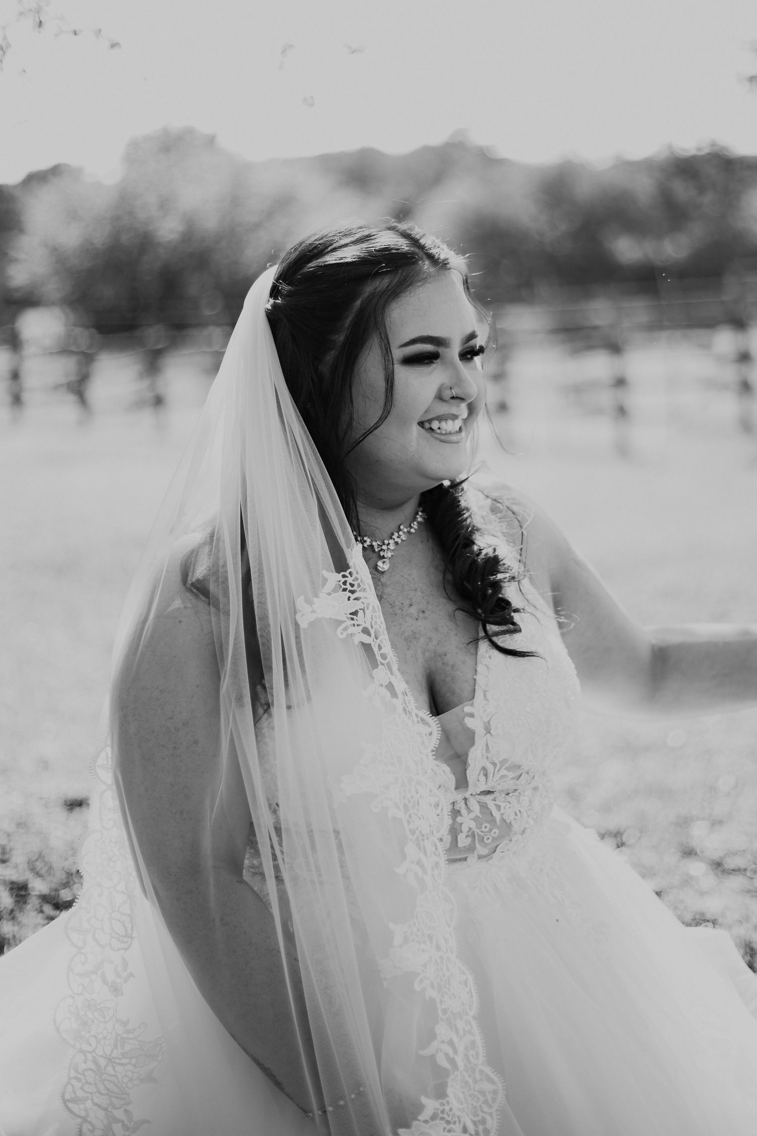 Black and white portrait of a joyful bride in a lace wedding dress and veil laughing during an outdoor photoshoot.