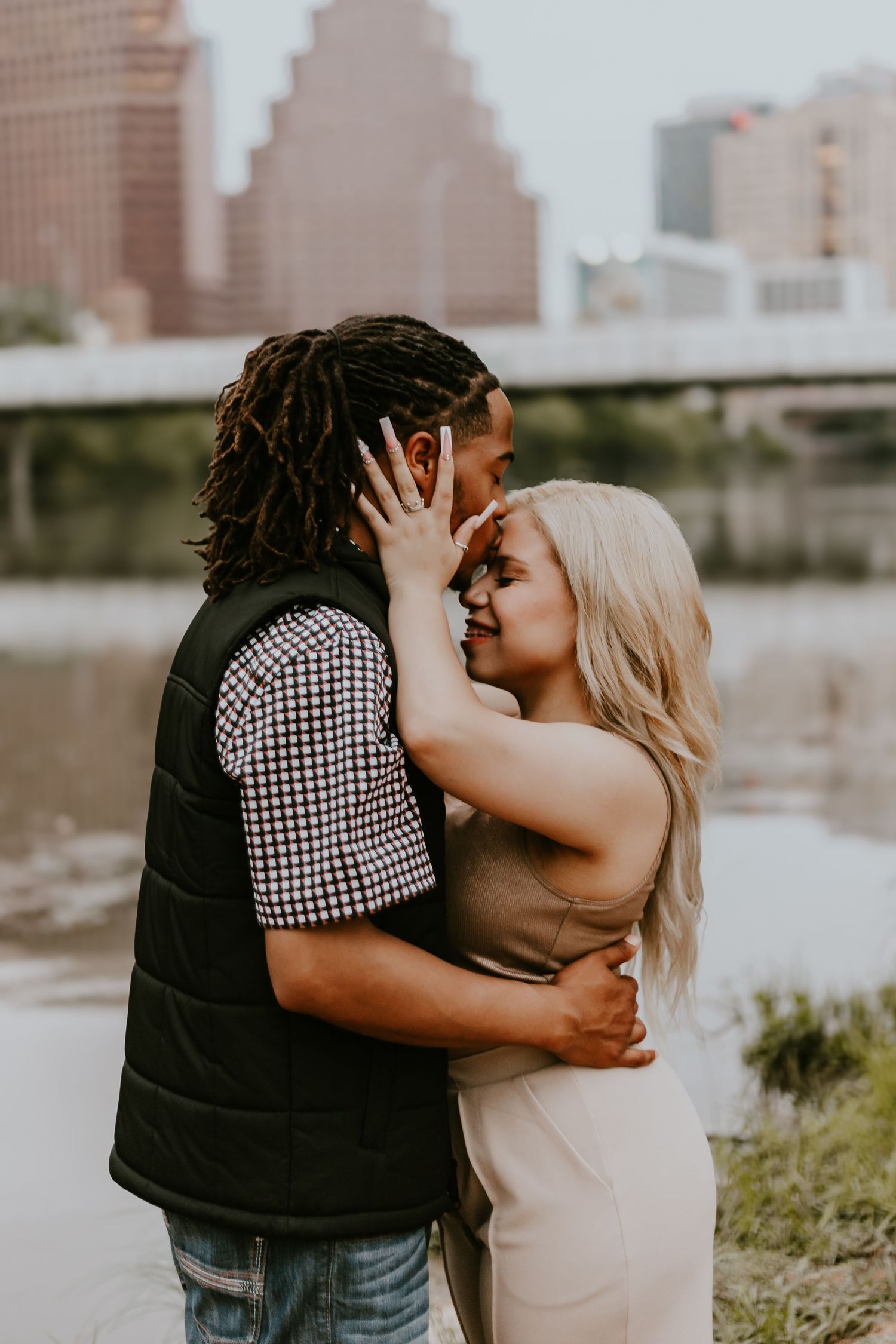 Intimate couple embracing outdoors with city skyline visible in background during golden hour.