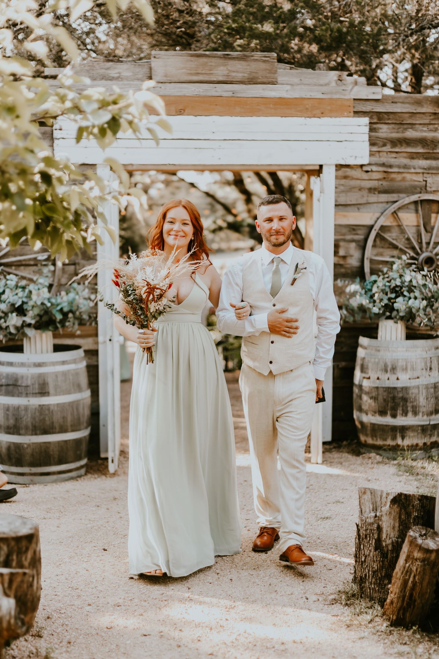 Rustic outdoor wedding ceremony set up with wooden barrels and arbor decorated in warm golden sunlight.