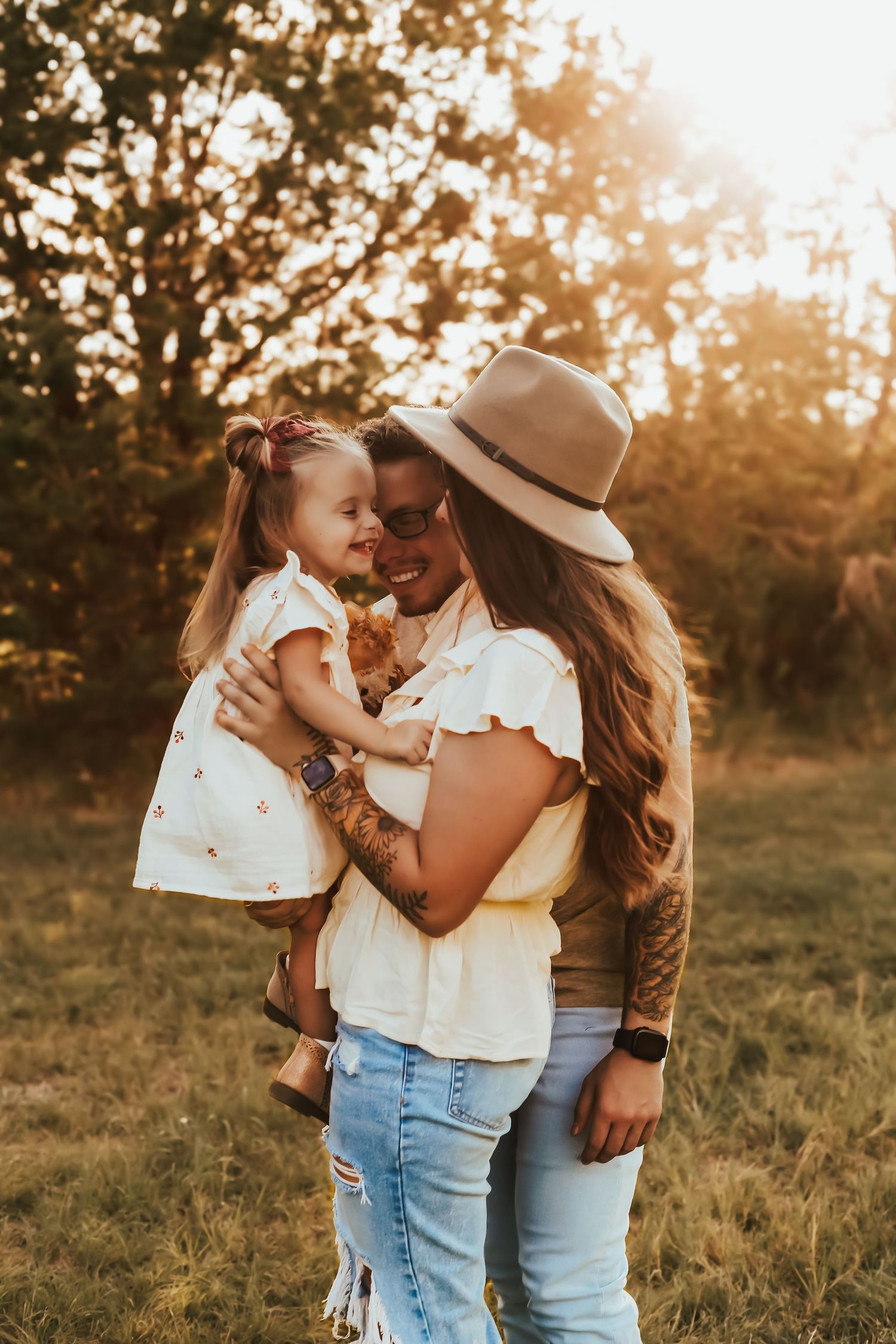 A loving embrace between family members in a sunlit field at golden hour wearing coordinated white and blue outfits.