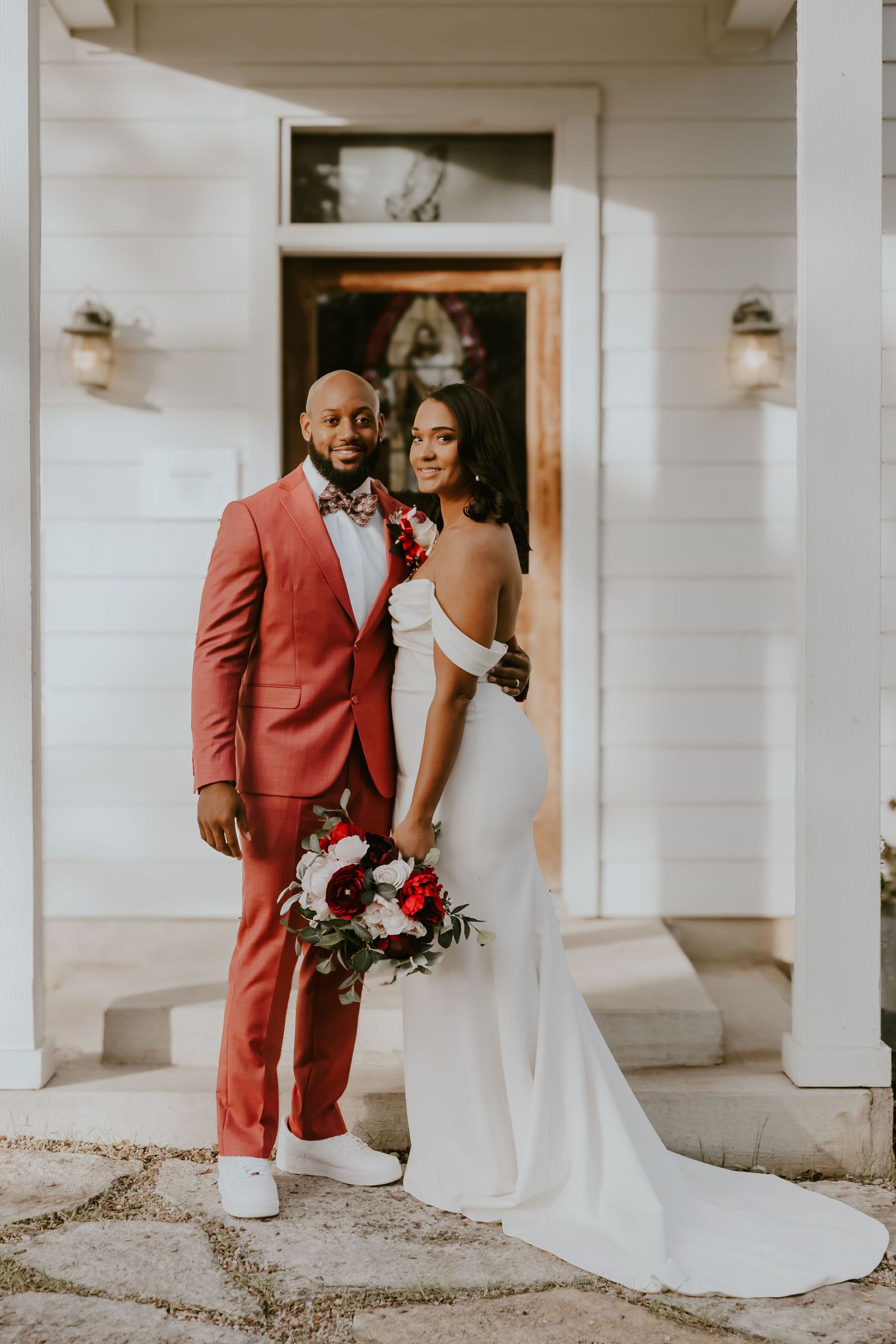 A bride and groom share an intimate moment in their wedding attire in front of a white building.
