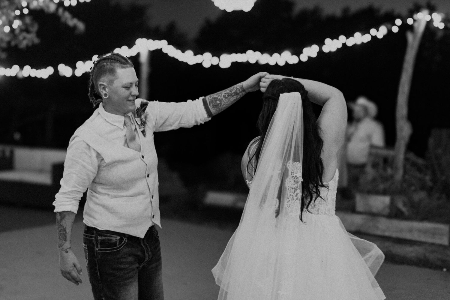 A couple dances at their wedding reception under string lights in a black and white photo.