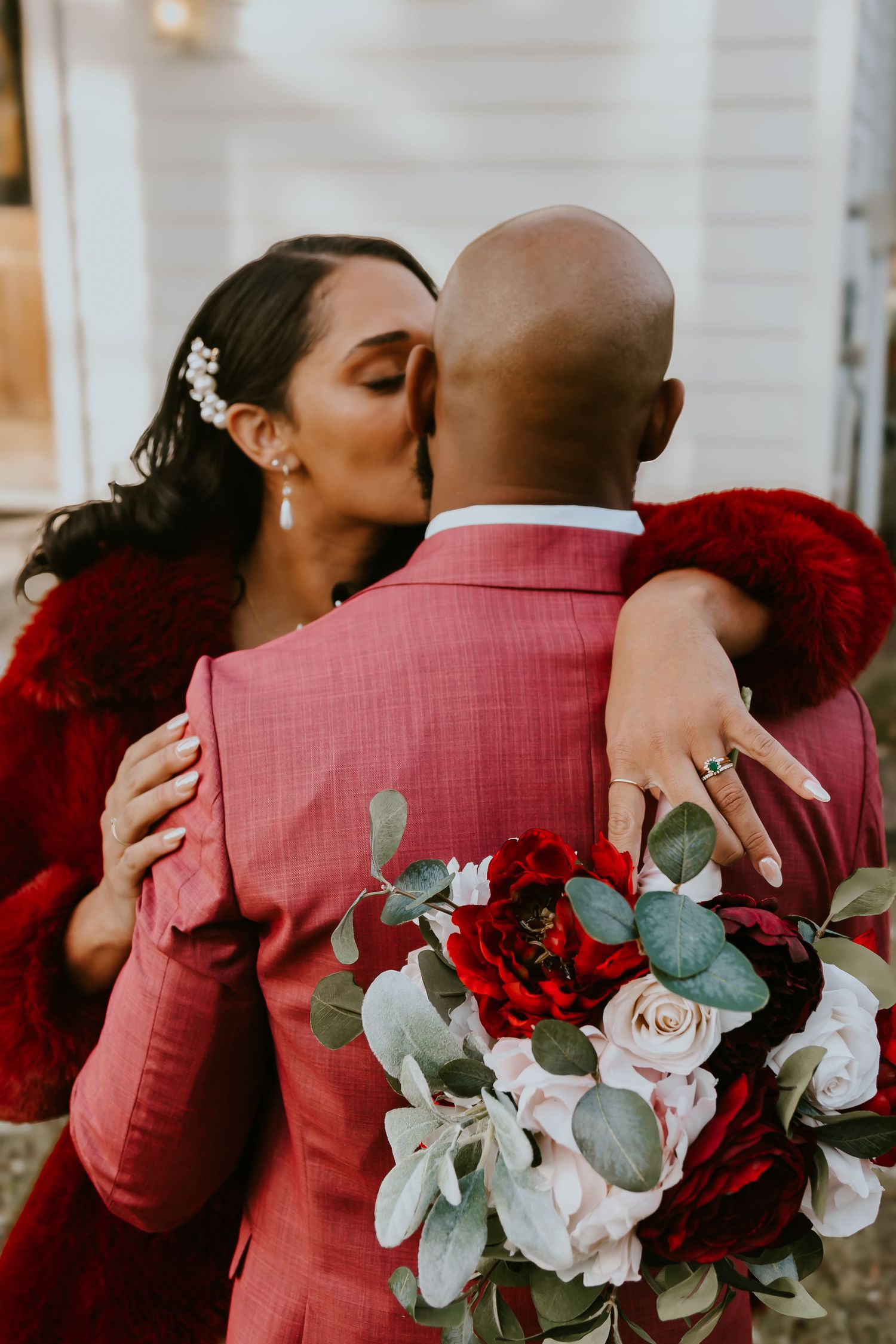 Romantic wedding moment with red and white bouquet featuring eucalyptus leaves and roses against pink attire.