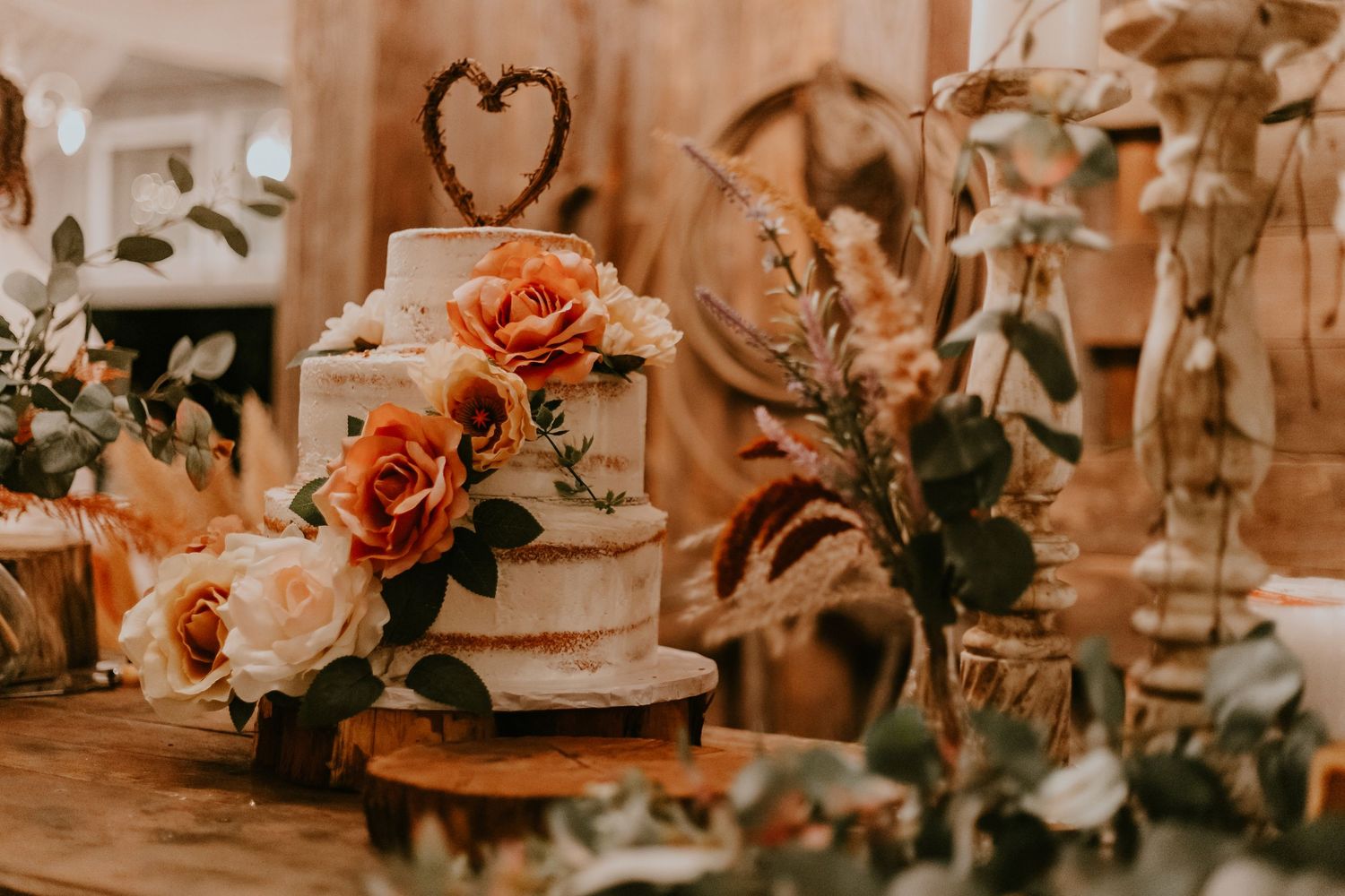Wedding reception table decorated with peach roses and white flowers around a tiered cake with heart topper.