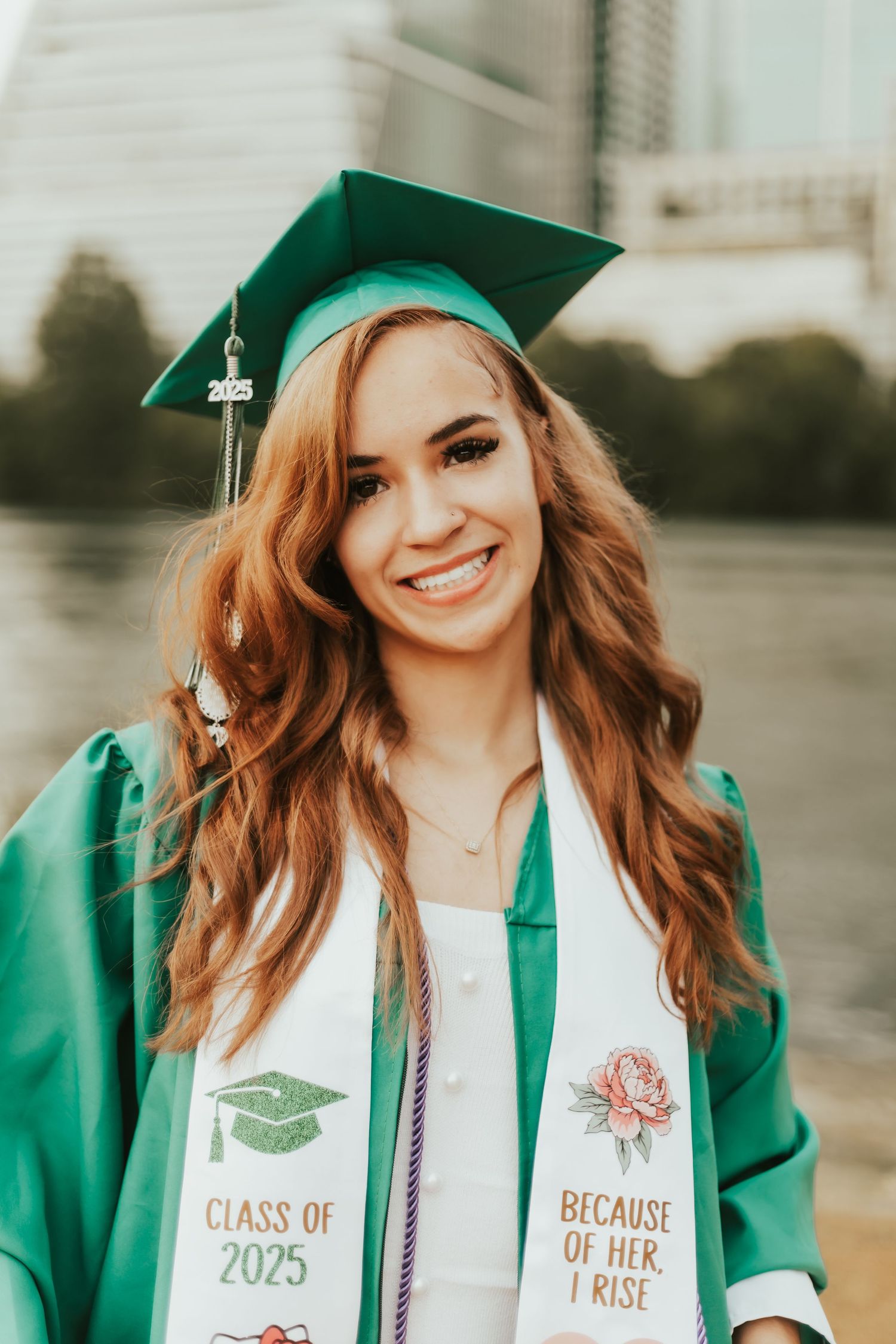 Graduate wearing emerald green cap and gown with decorated white stole showing Class of 2025 at outdoor ceremony.