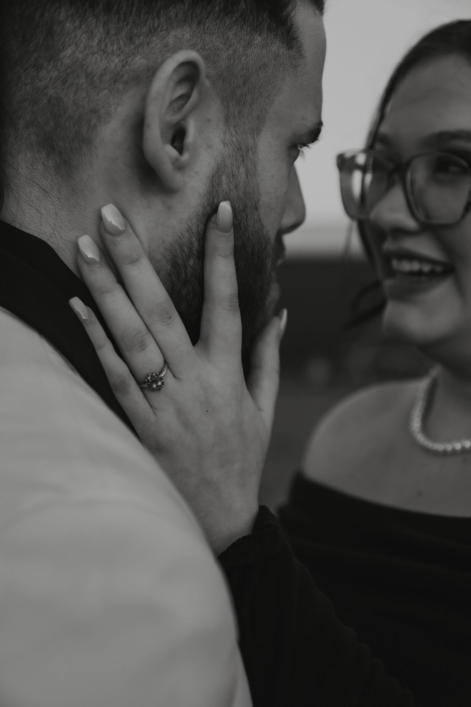 Black and white close-up photo showing a heartfelt candid moment with one wearing glasses and a pearl necklace.