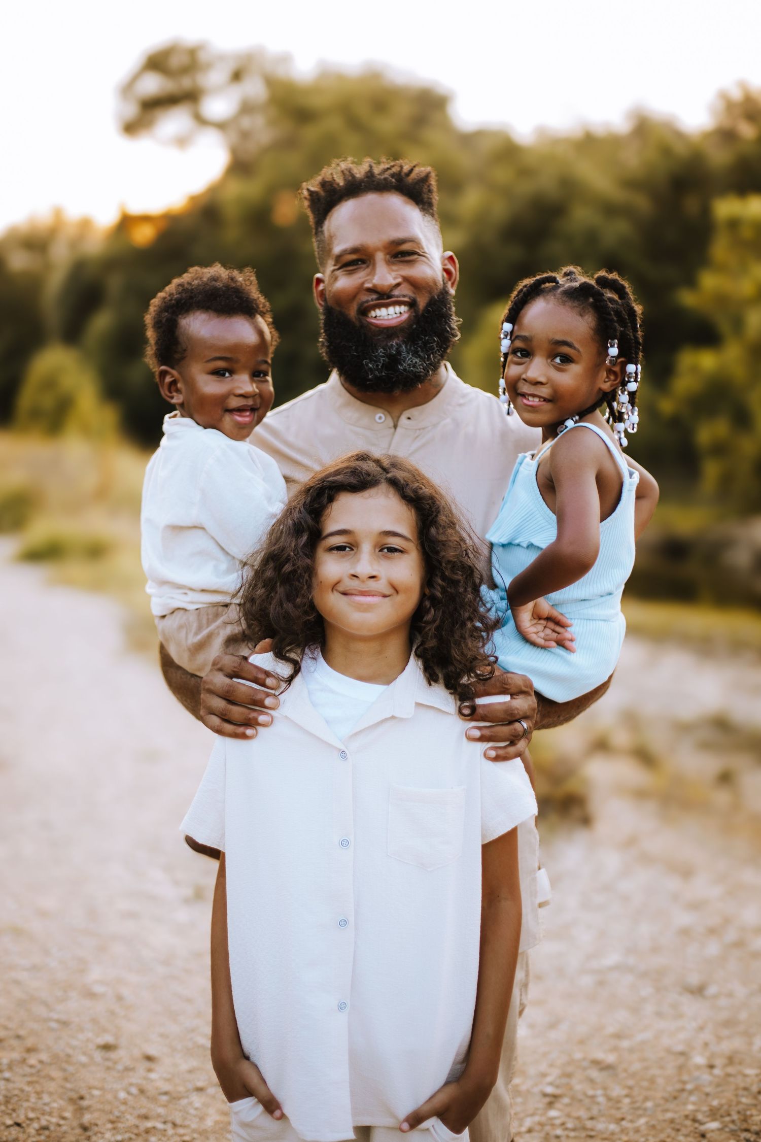 A happy family of four poses together on a dirt path during golden hour in nature.